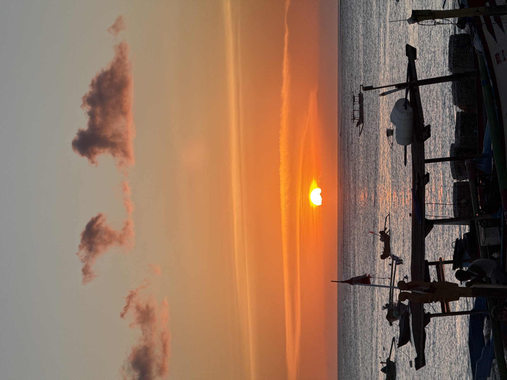 Airplane crosses sun during Kuta sunset with boats below