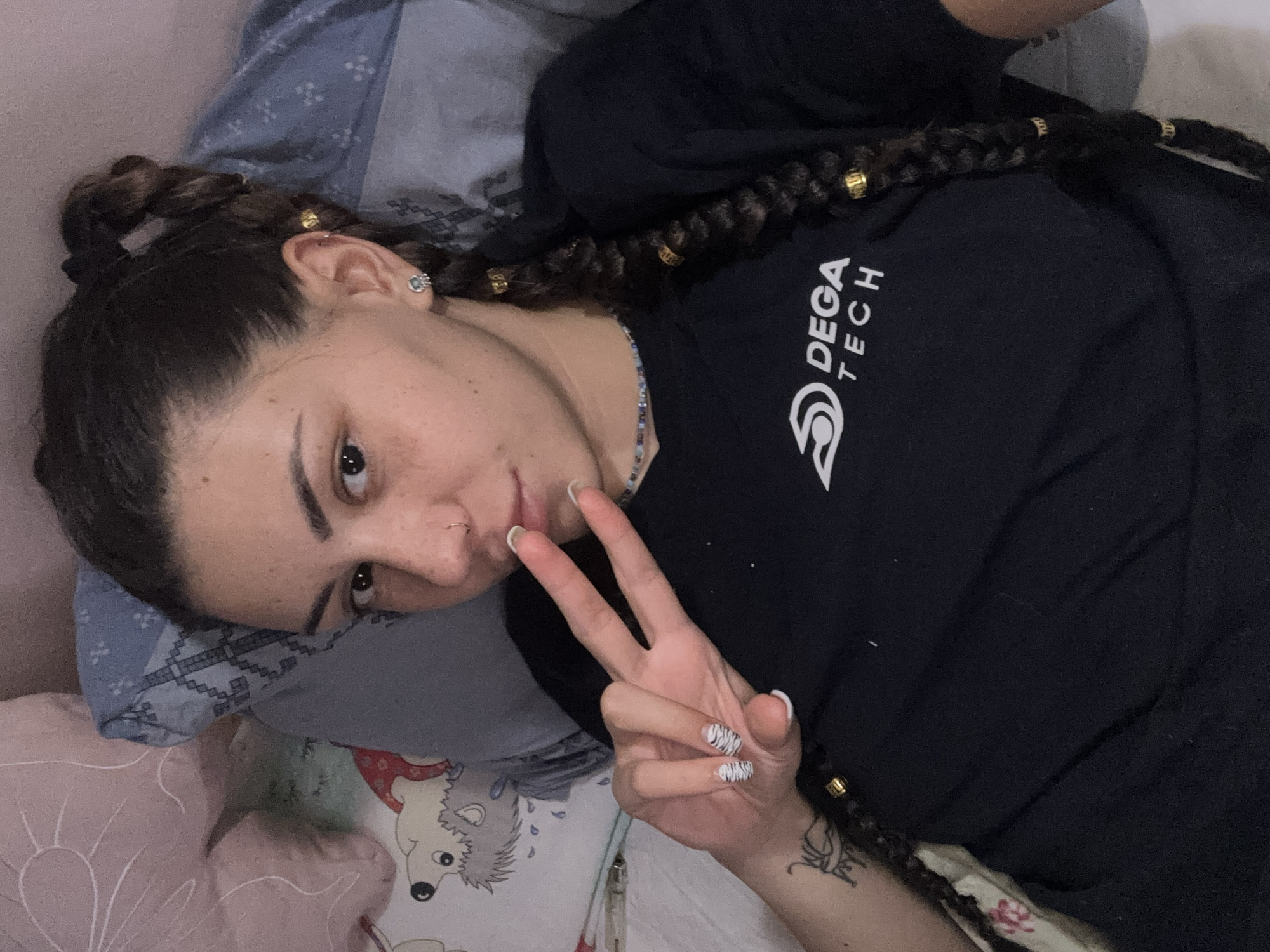 Relaxed bedroom pose with braids, gold beads, and a peace sign.