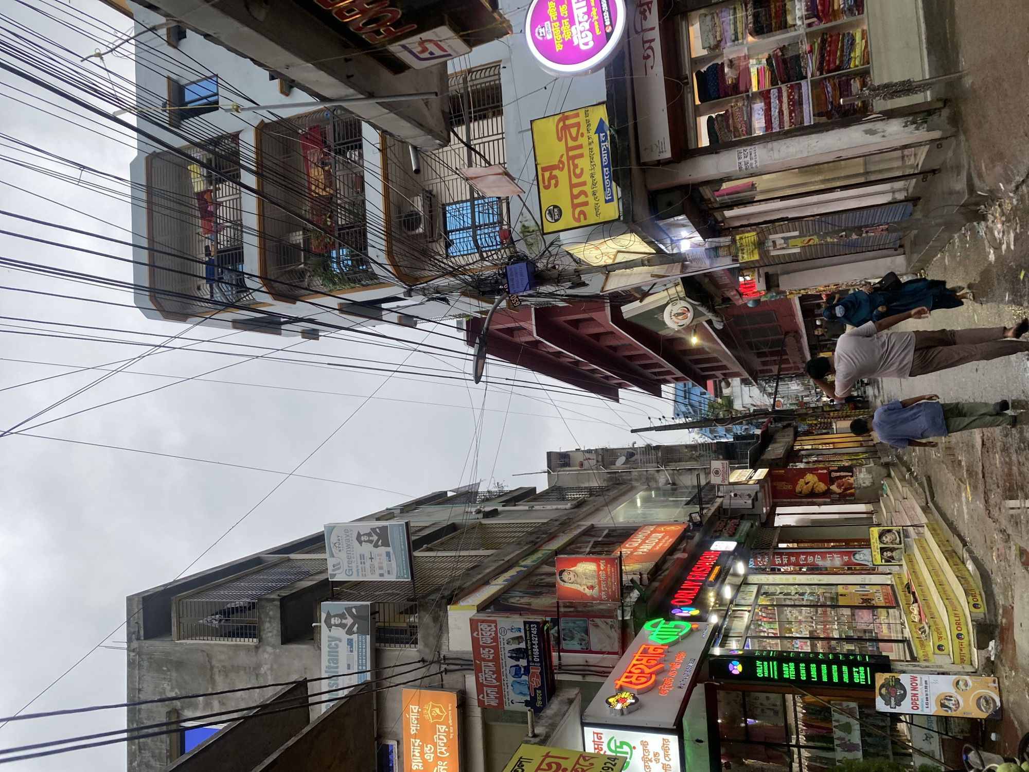Busy Dhaka street: chaotic wiring overhead, snack stall below