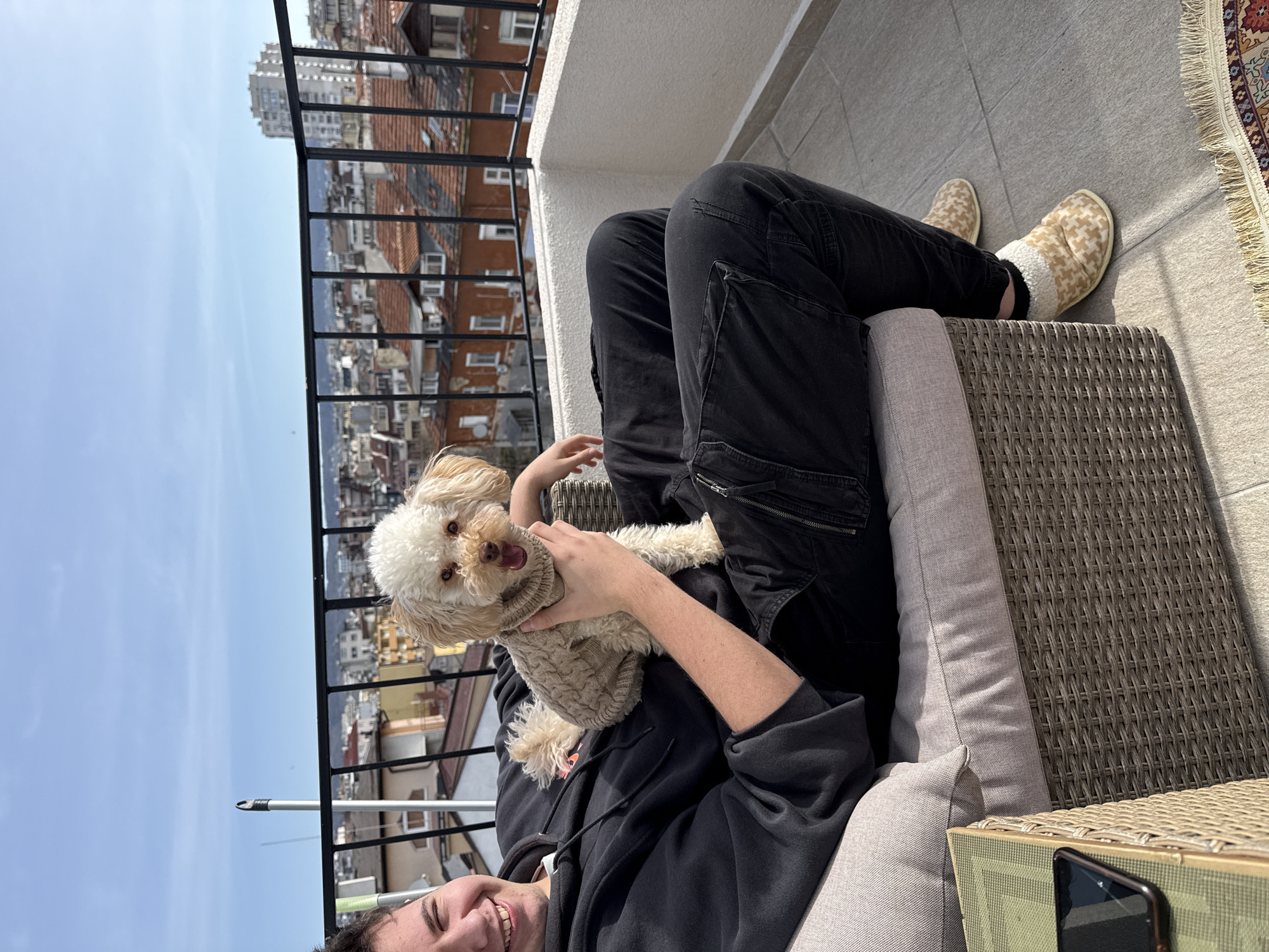 Person holds sweater-clad dog on Varna balcony morning scene