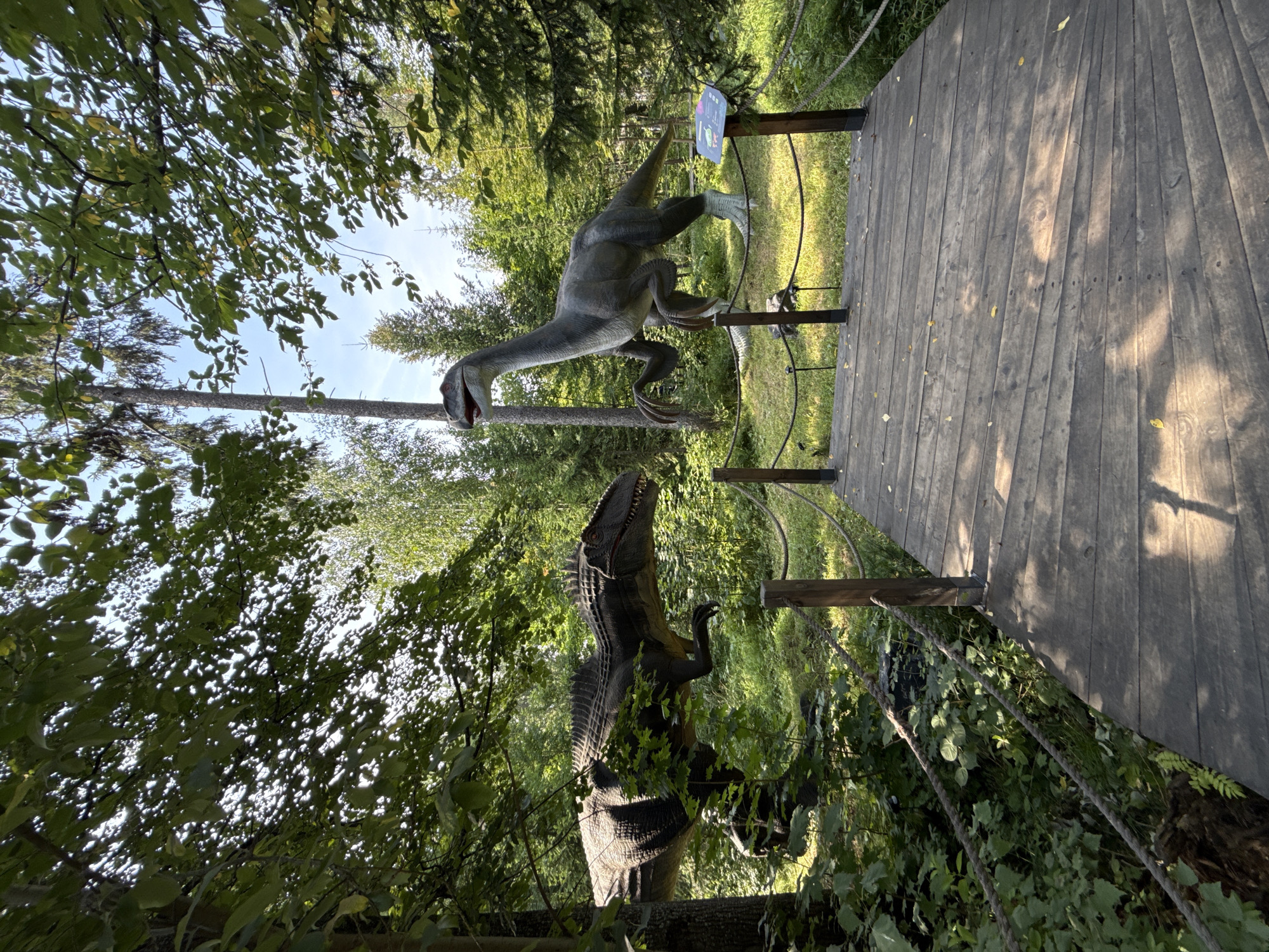 Life-sized dinosaur models on a wooded trail at Izhevsk Zoo