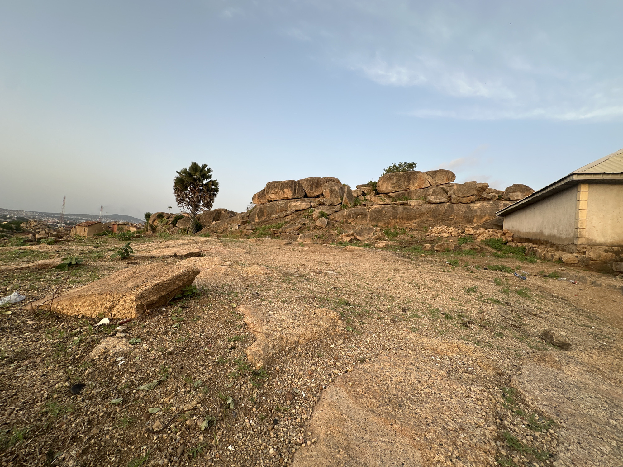 Two people overlook Jos settlement from rocky hilltop at sunset