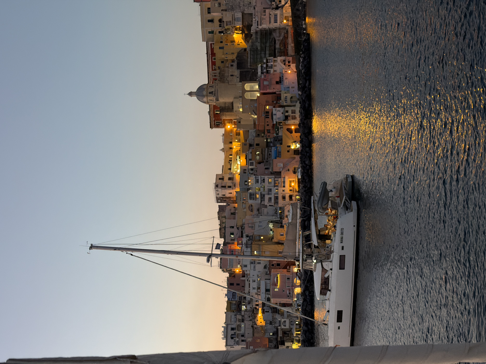 White sailboat docks at Procida harbor during dusk