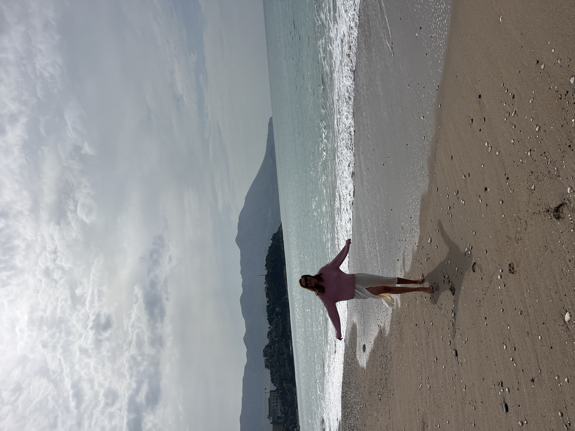 Woman spreads arms on Budva beach overlooking Adriatic Sea