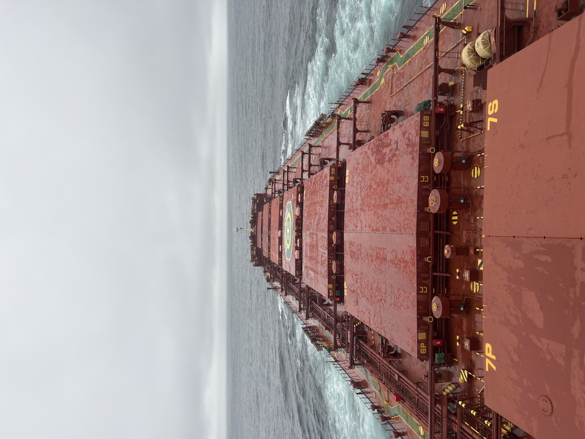 Cargo ship navigates rough gray seas under heavy overcast