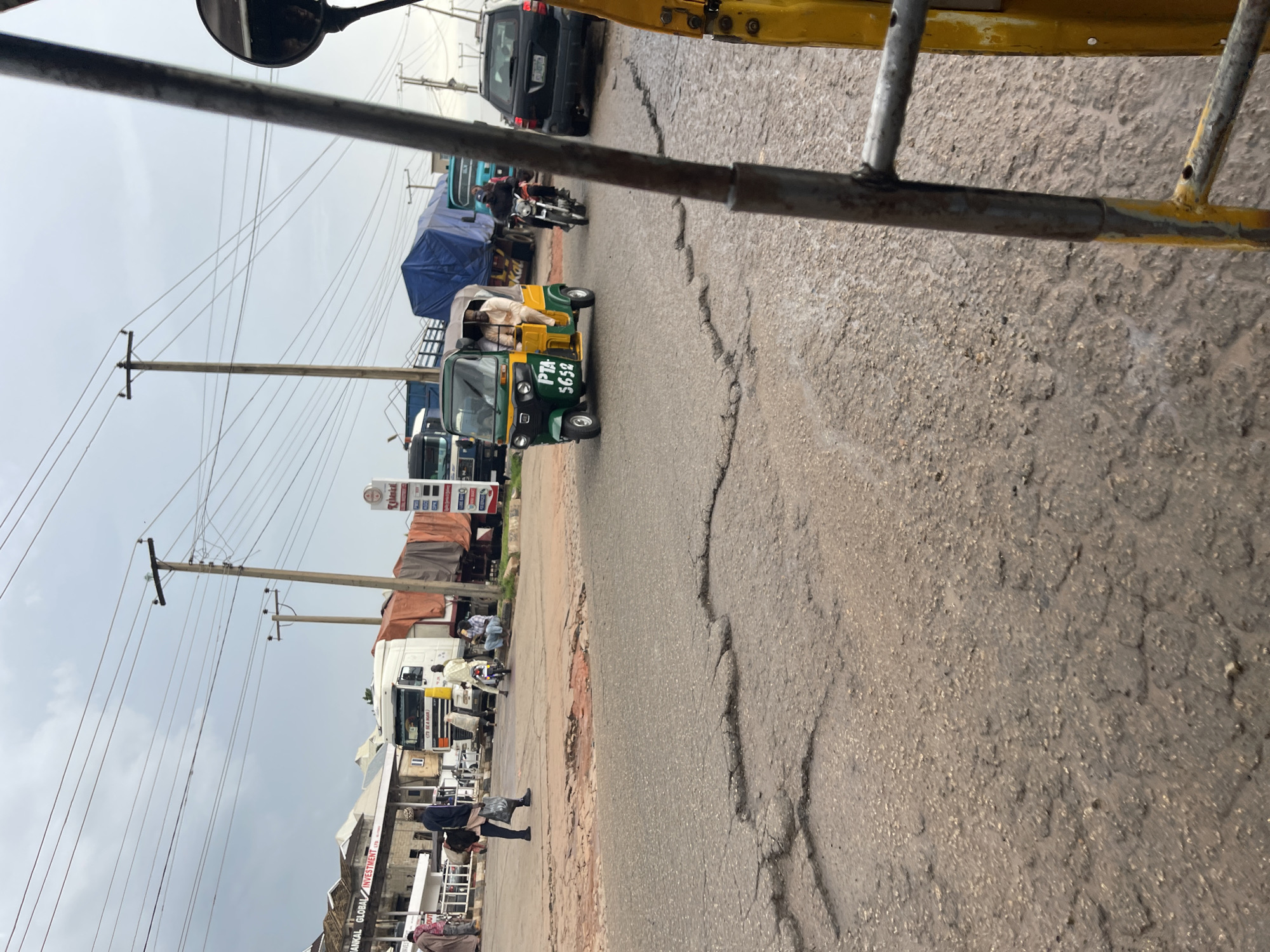 Keke napeps navigate Jos's wet, potholed streets on a cloudy afternoon