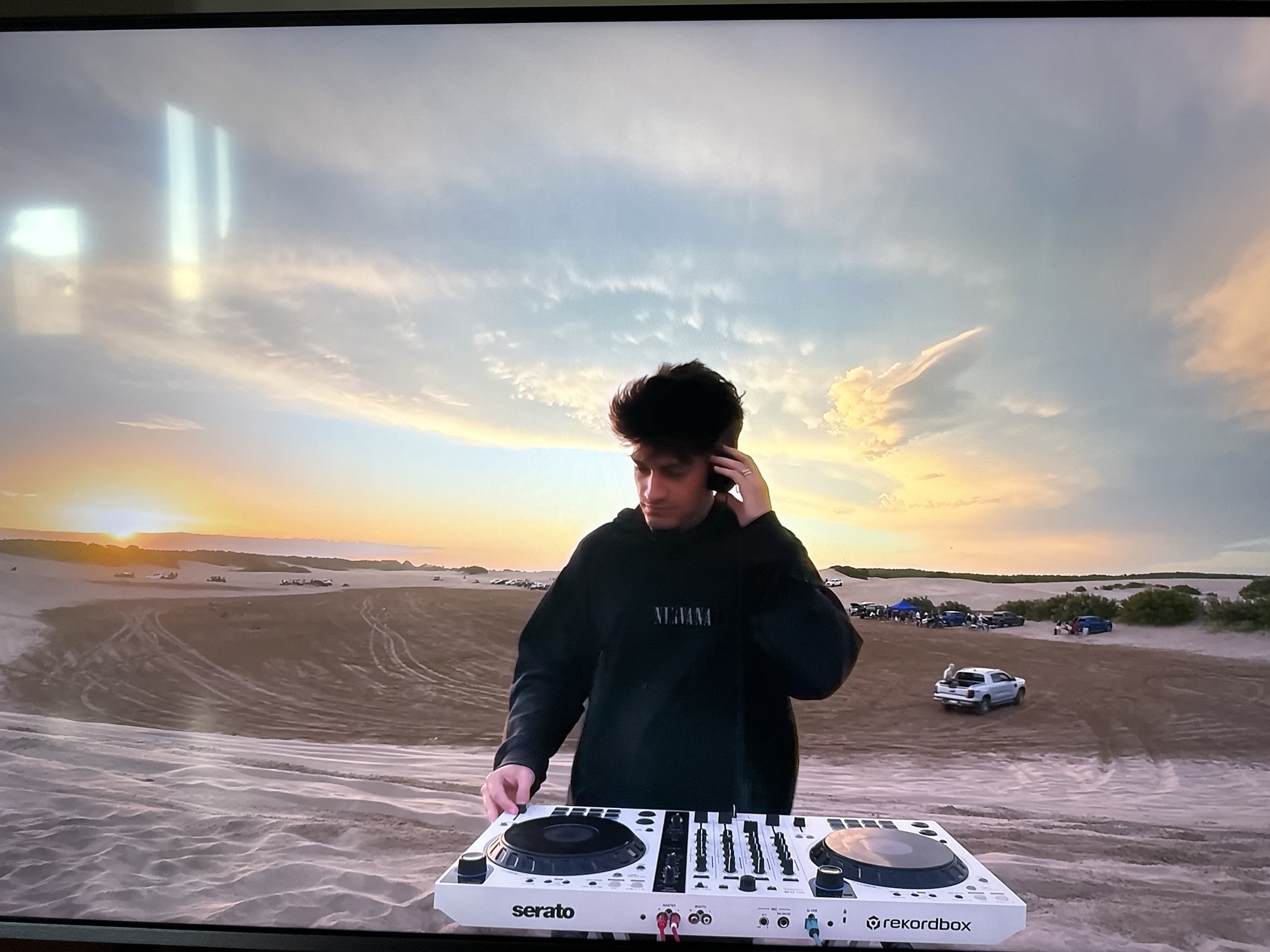 DJ performs with controller in sandy outdoor setting at sunset