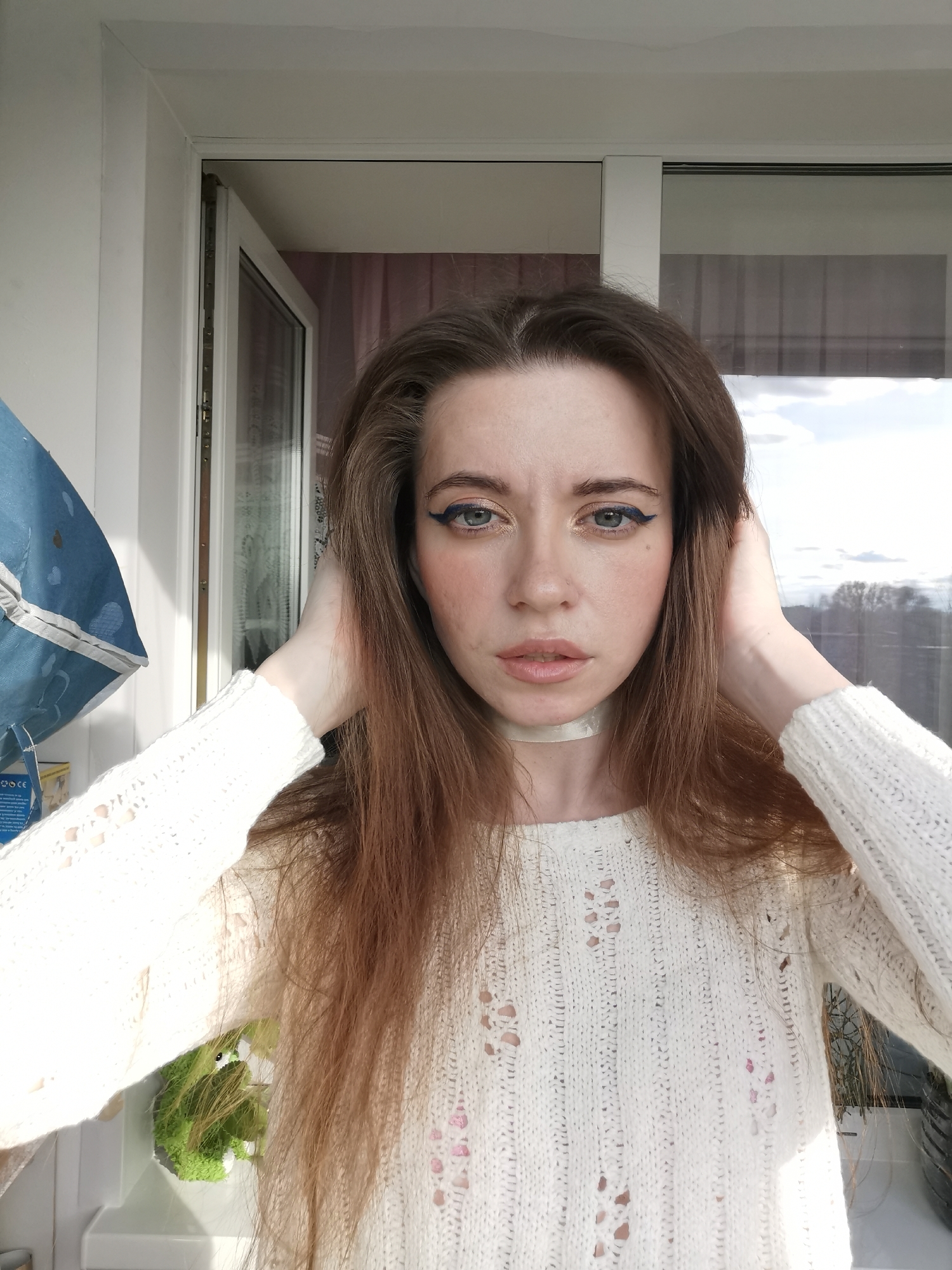 Woman takes selfies by window in white sweater