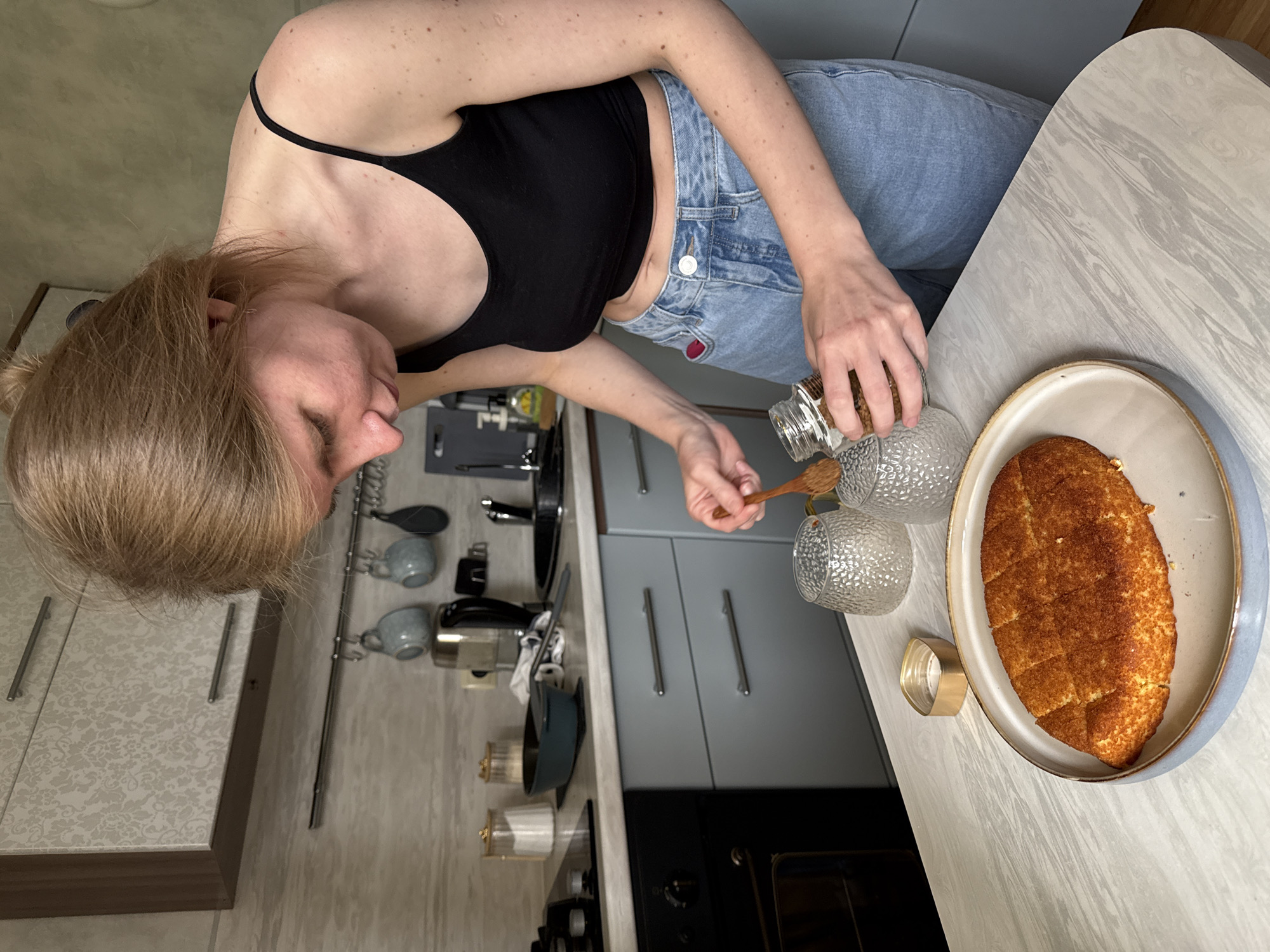 Woman transfers jar contents with wooden spoon in Izhevsk kitchen