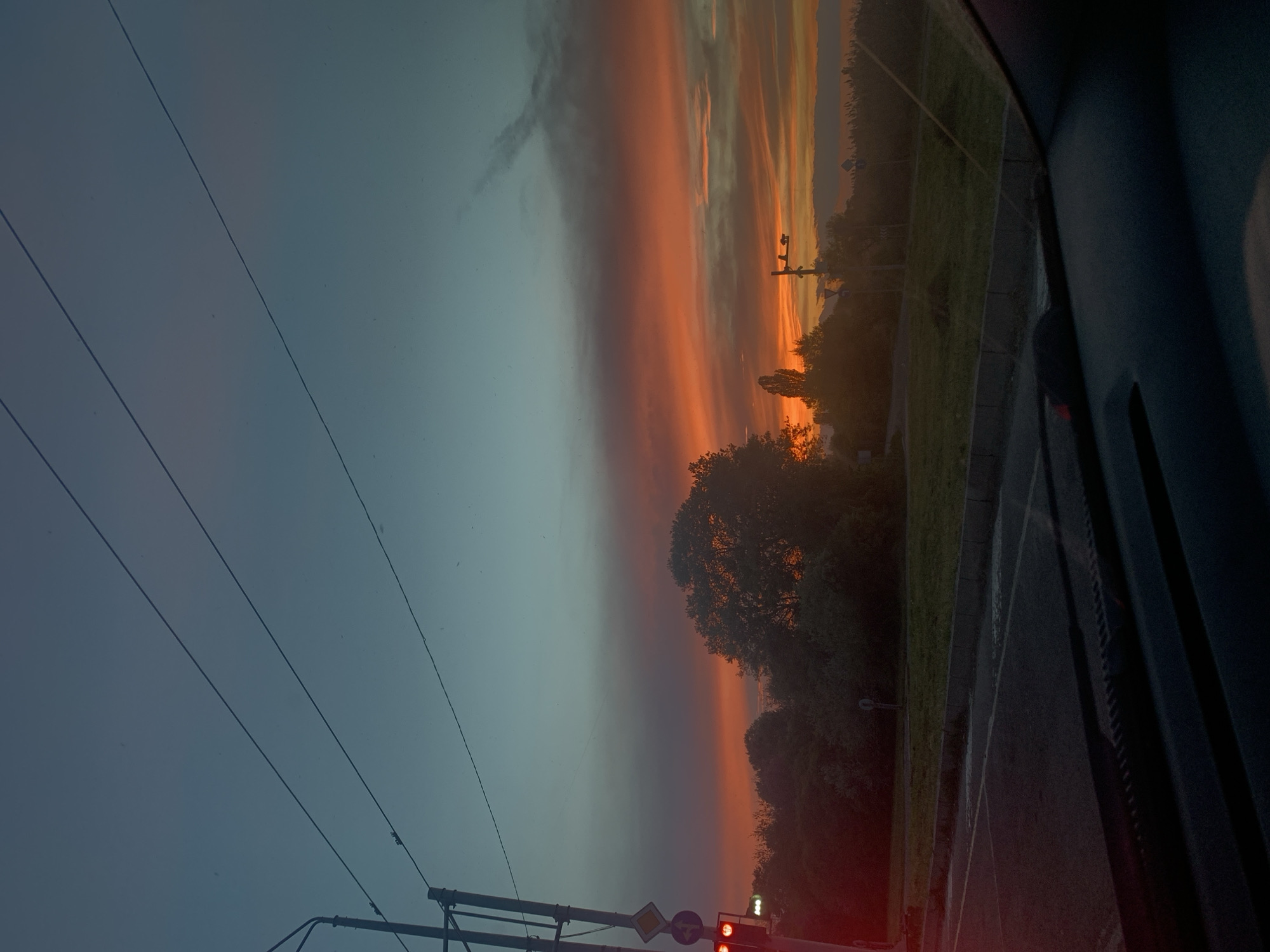 Driver captures colorful sunset view along tree-lined road