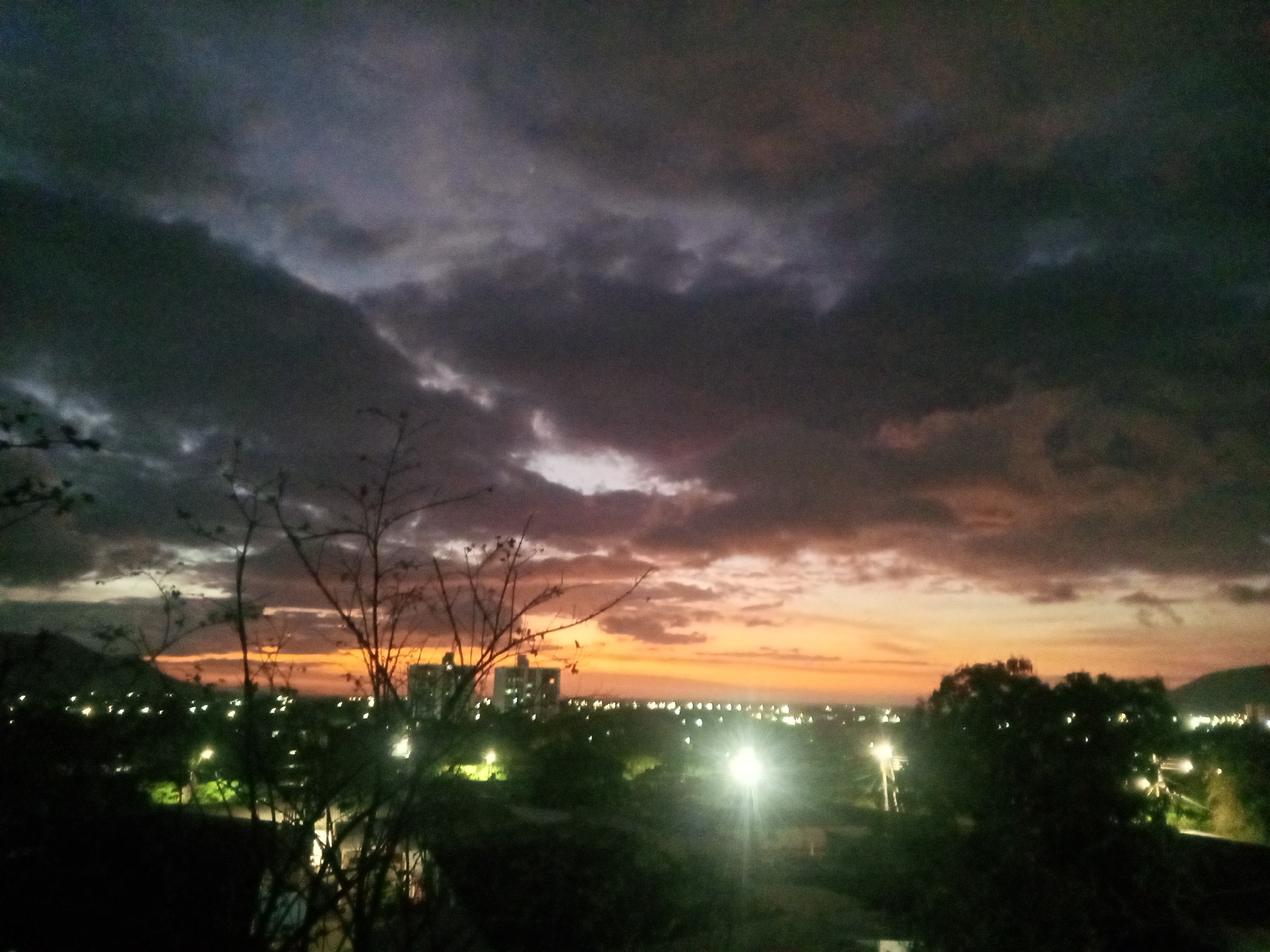 Urban sunset creates orange purple sky through dark clouds