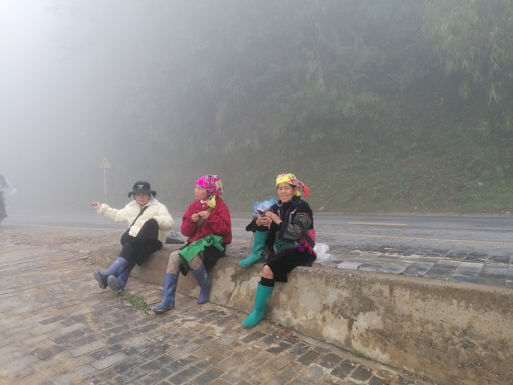 Three women sit on roadside wall