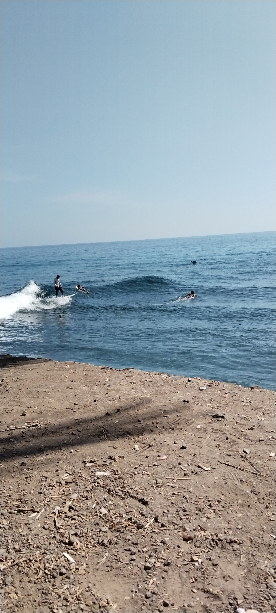 Surfers in the water off Senggigi's rocky coastline
