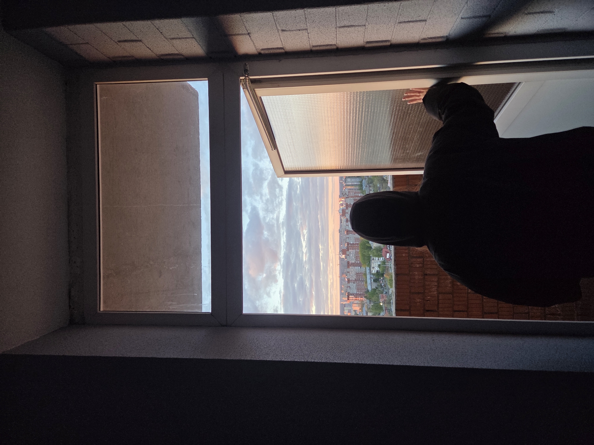 Person watches sunset from Perm rooftop while using smartphone