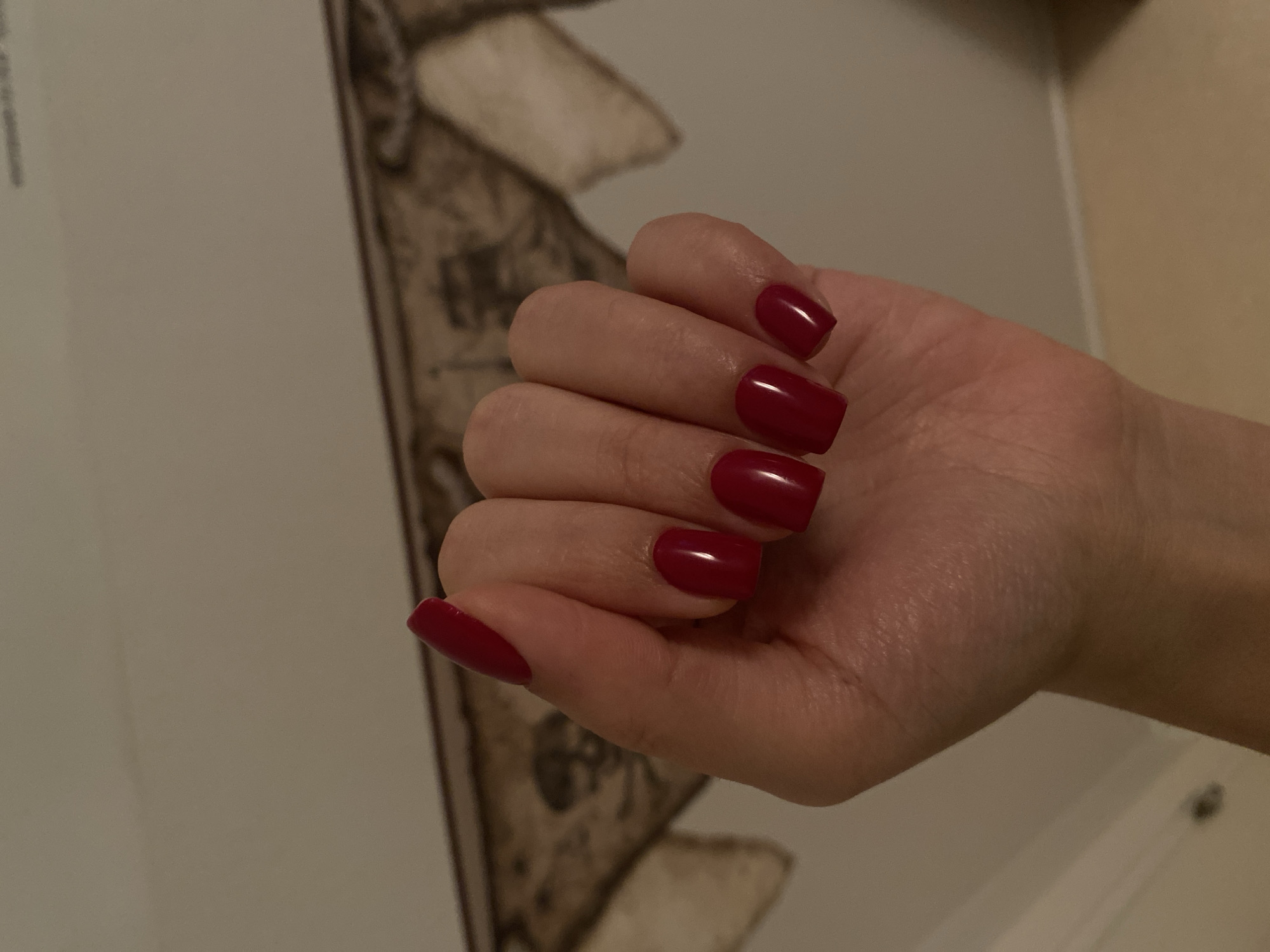 Red square nails photographed against pirate-themed wall art