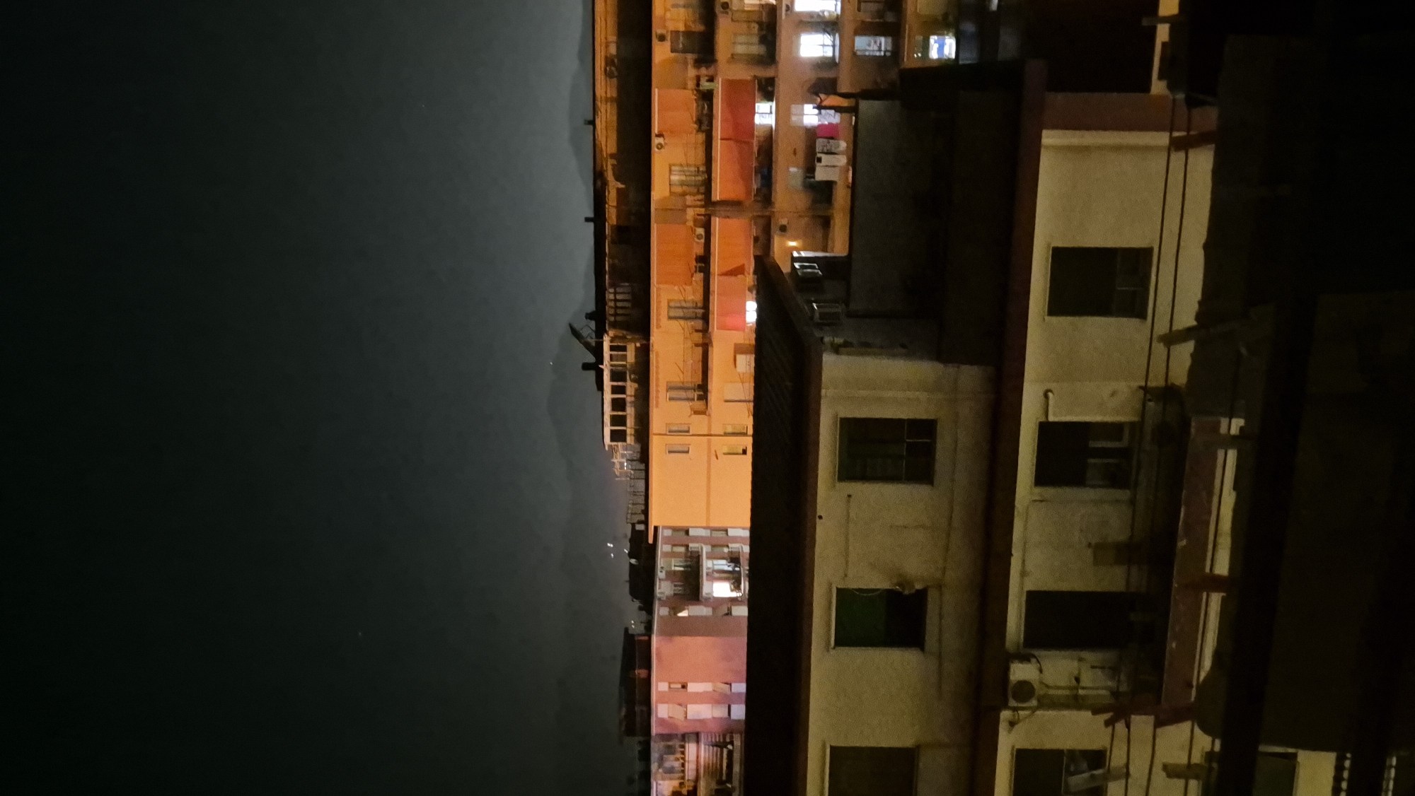City apartment blocks lit up at night, hills in the distance