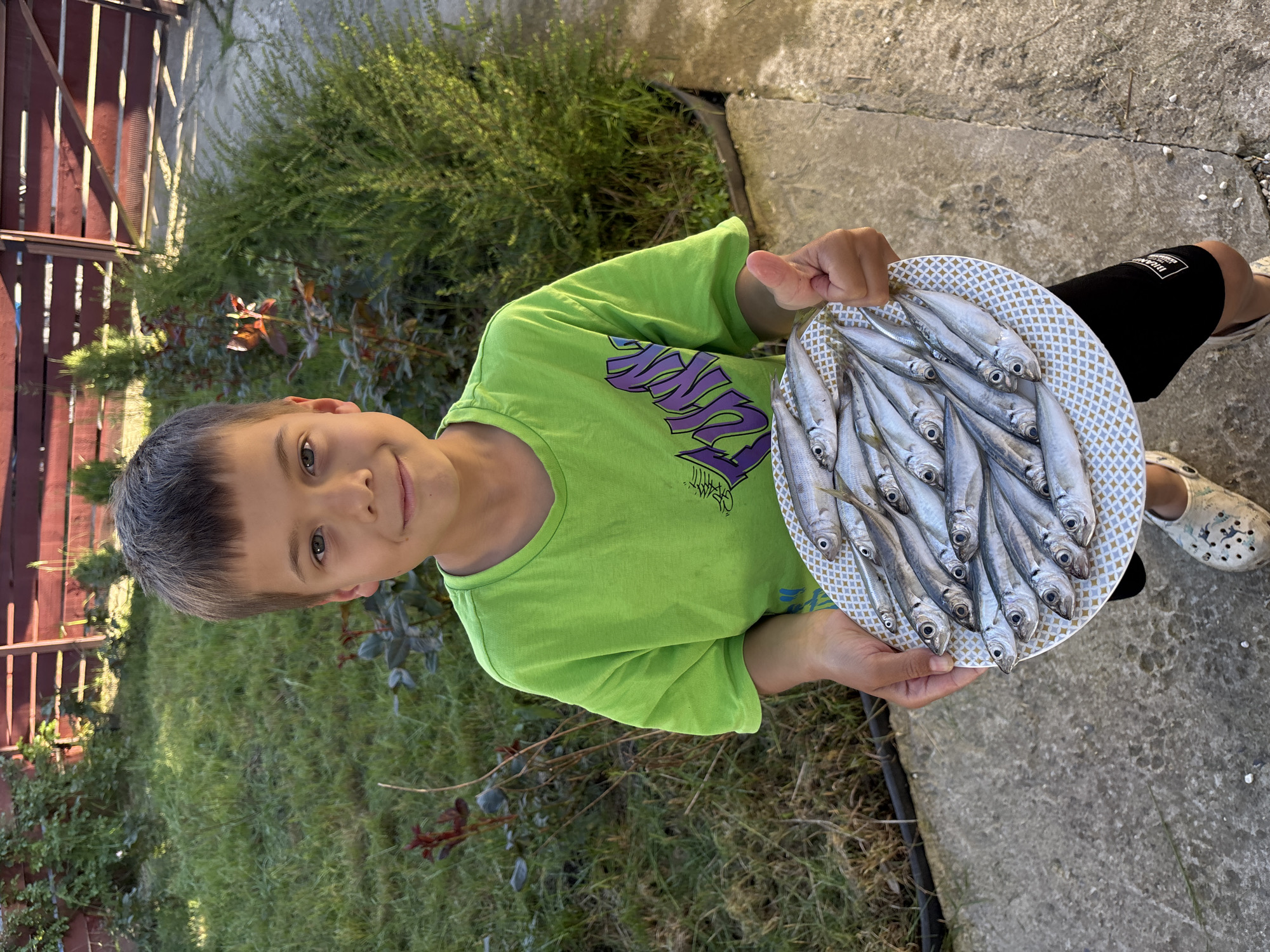 Boy displays fresh catch on plate in Plastunka yard