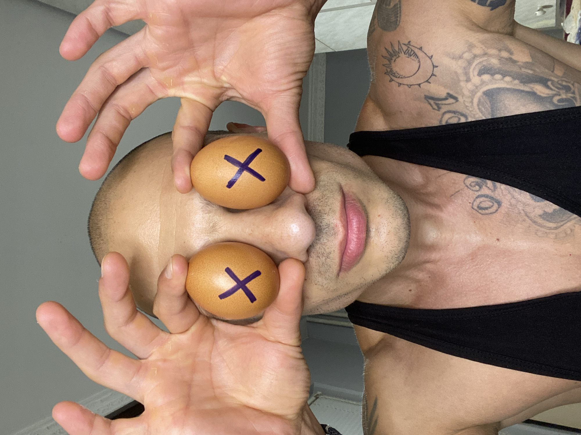 Tattooed person holds X-marked eggs over their eyes in Pleven