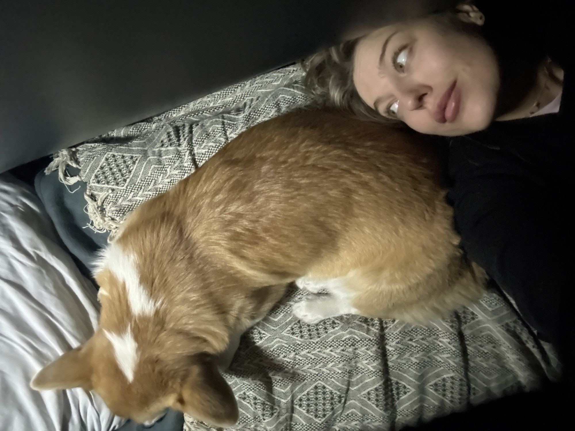 Woman rests with corgi on bed in Russia