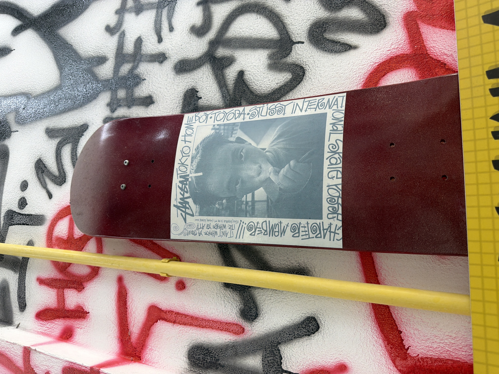 Skateboard with sticker spotted on graffitied wall in Chalong