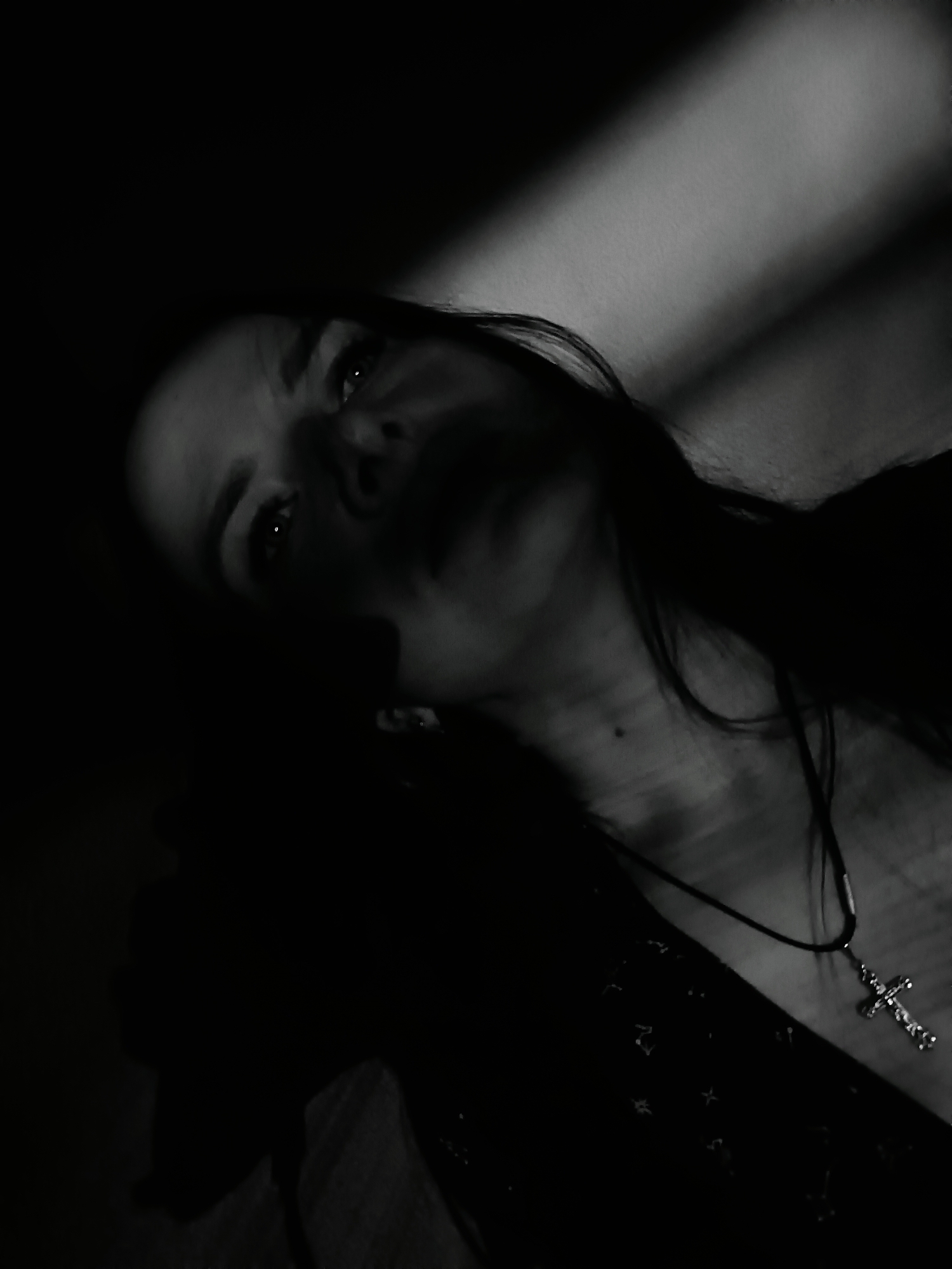 Person photographed in dramatic lighting wearing cross pendant