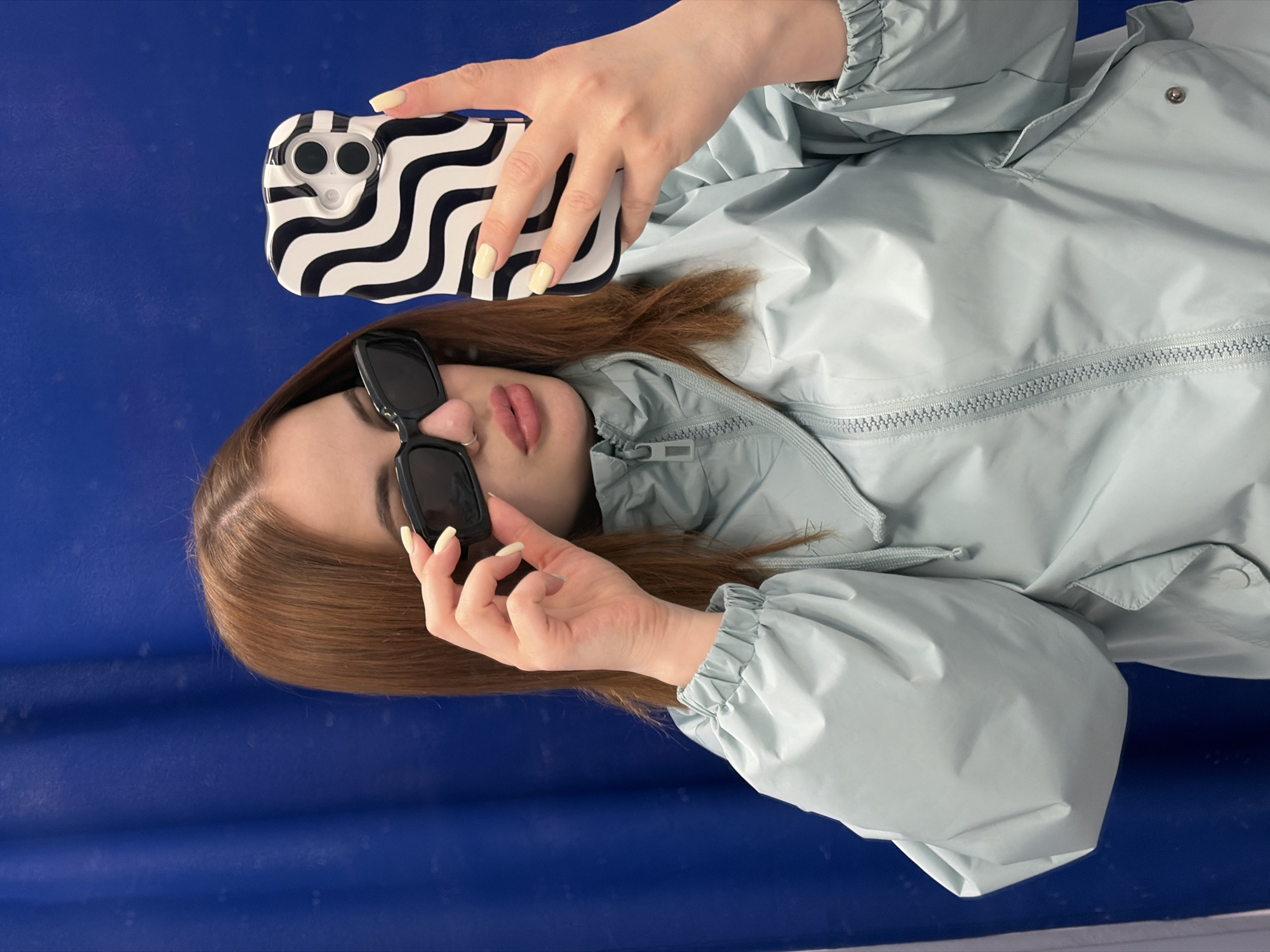 Woman in blue jacket takes outdoor selfies, adjusts sunglasses