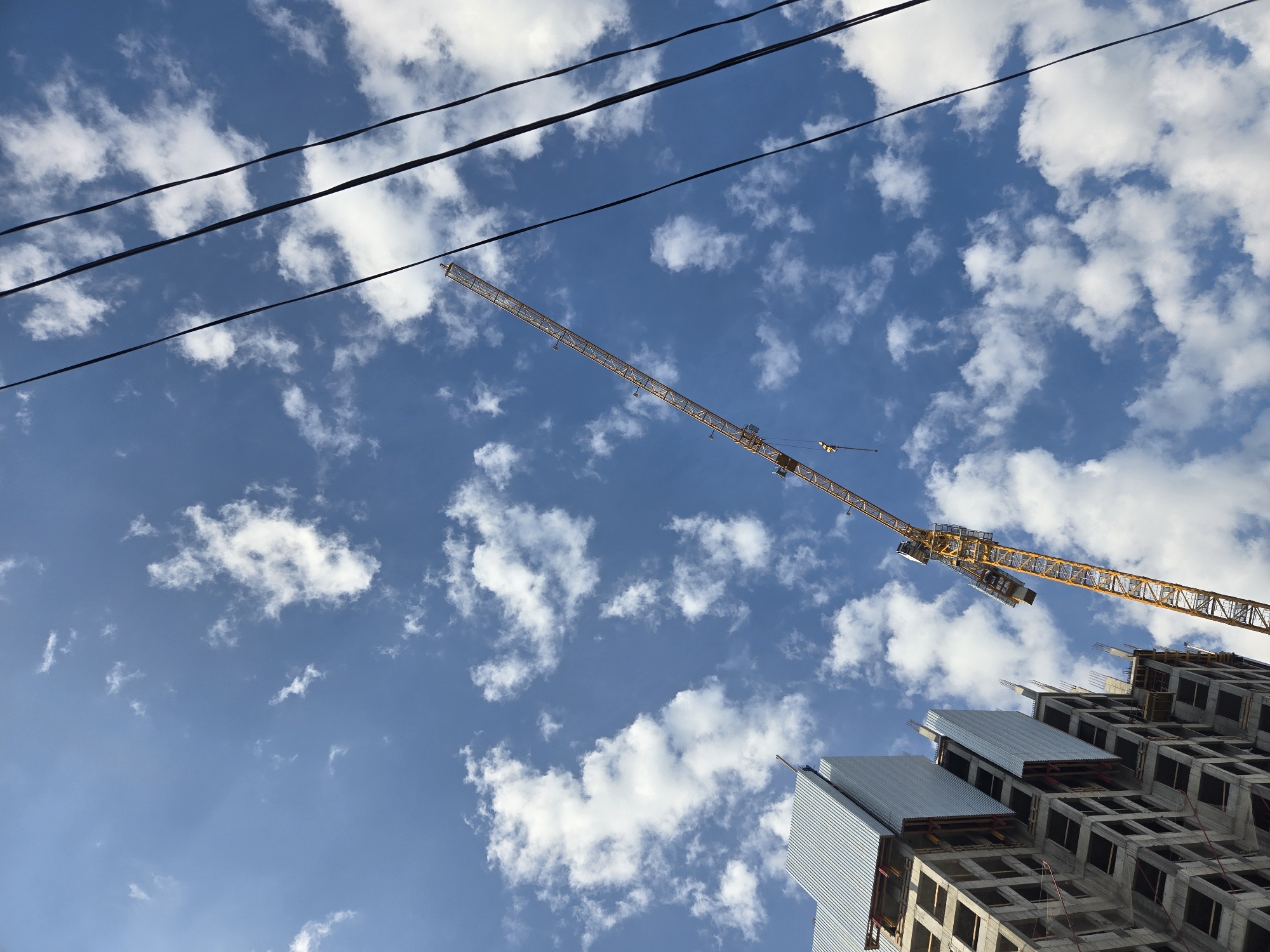 Tall building mid-construction, yellow crane against blue sky