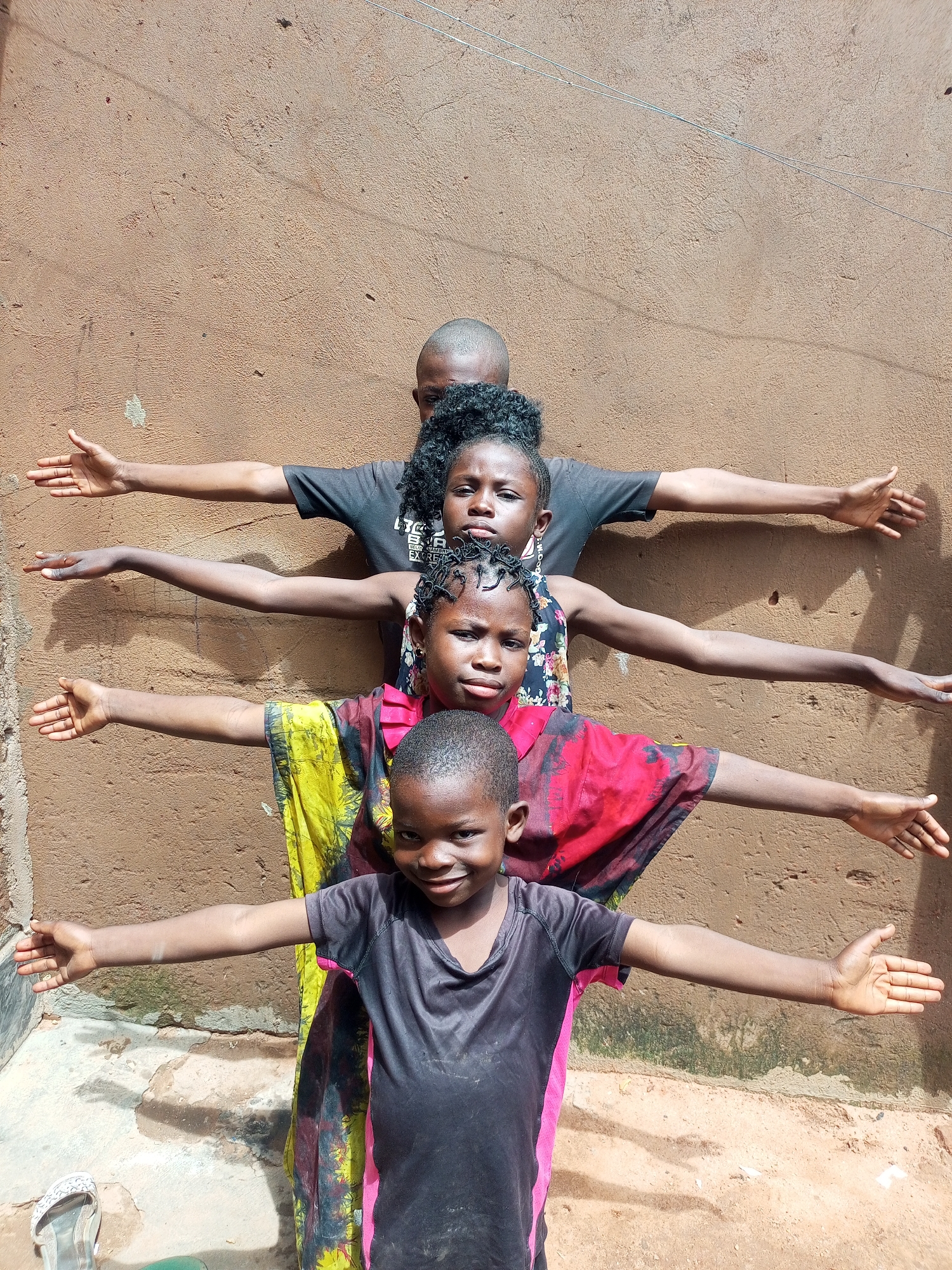 Four kids line up with arms outstretched against a tan wall