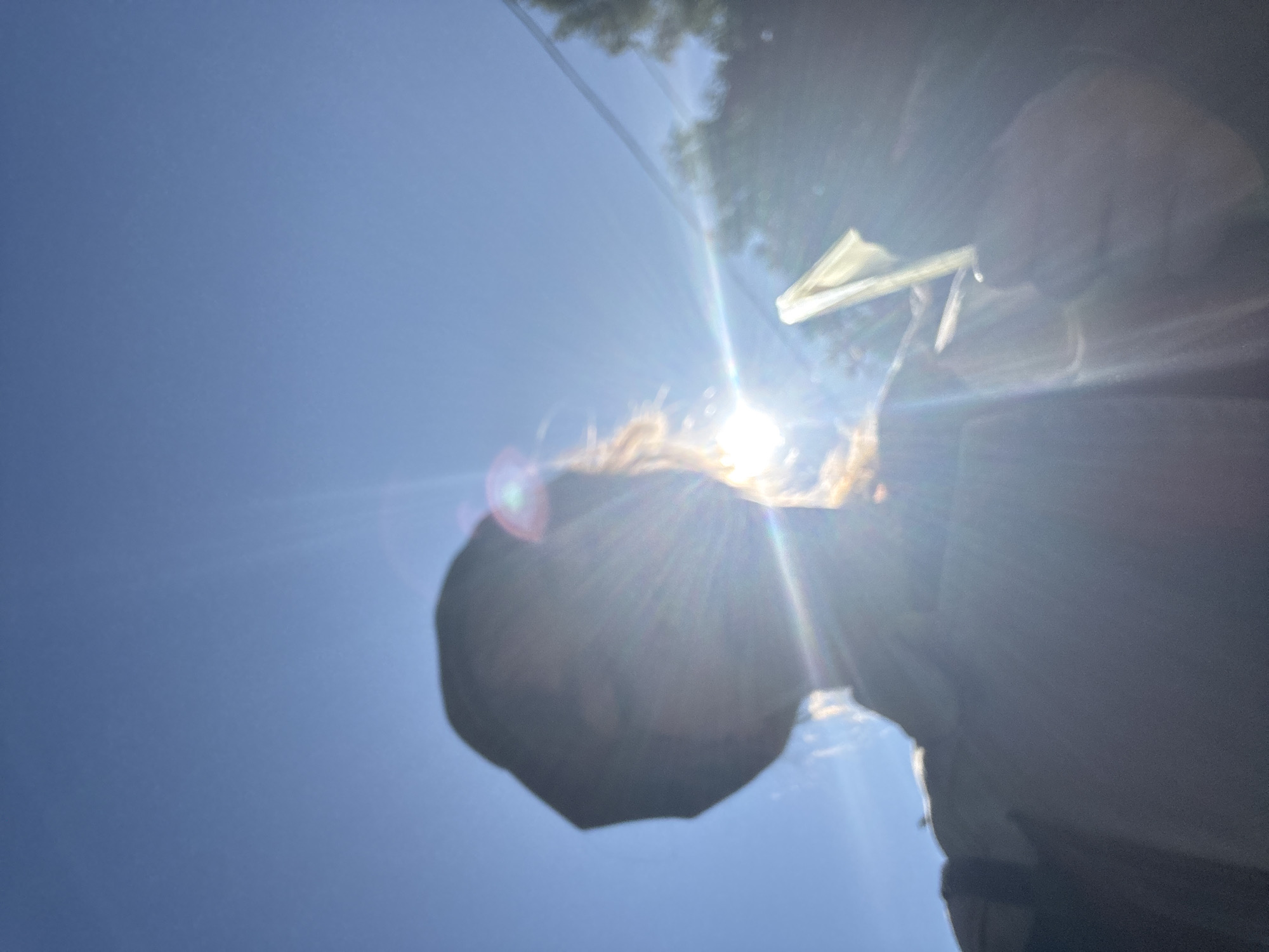 Silhouette holds folded paper against sun-flared blue sky