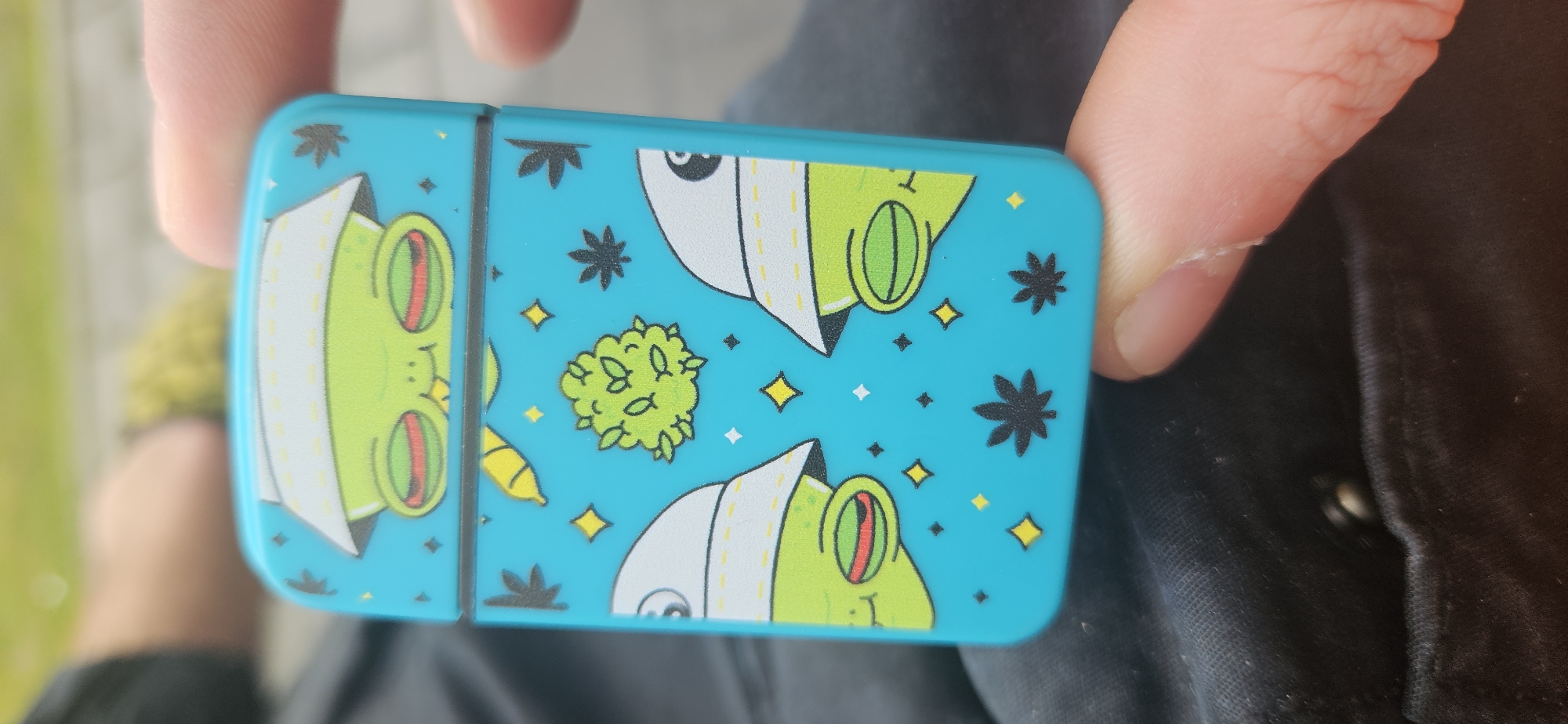 Person holds cannabis-themed container with cartoon frogs in Plovdiv