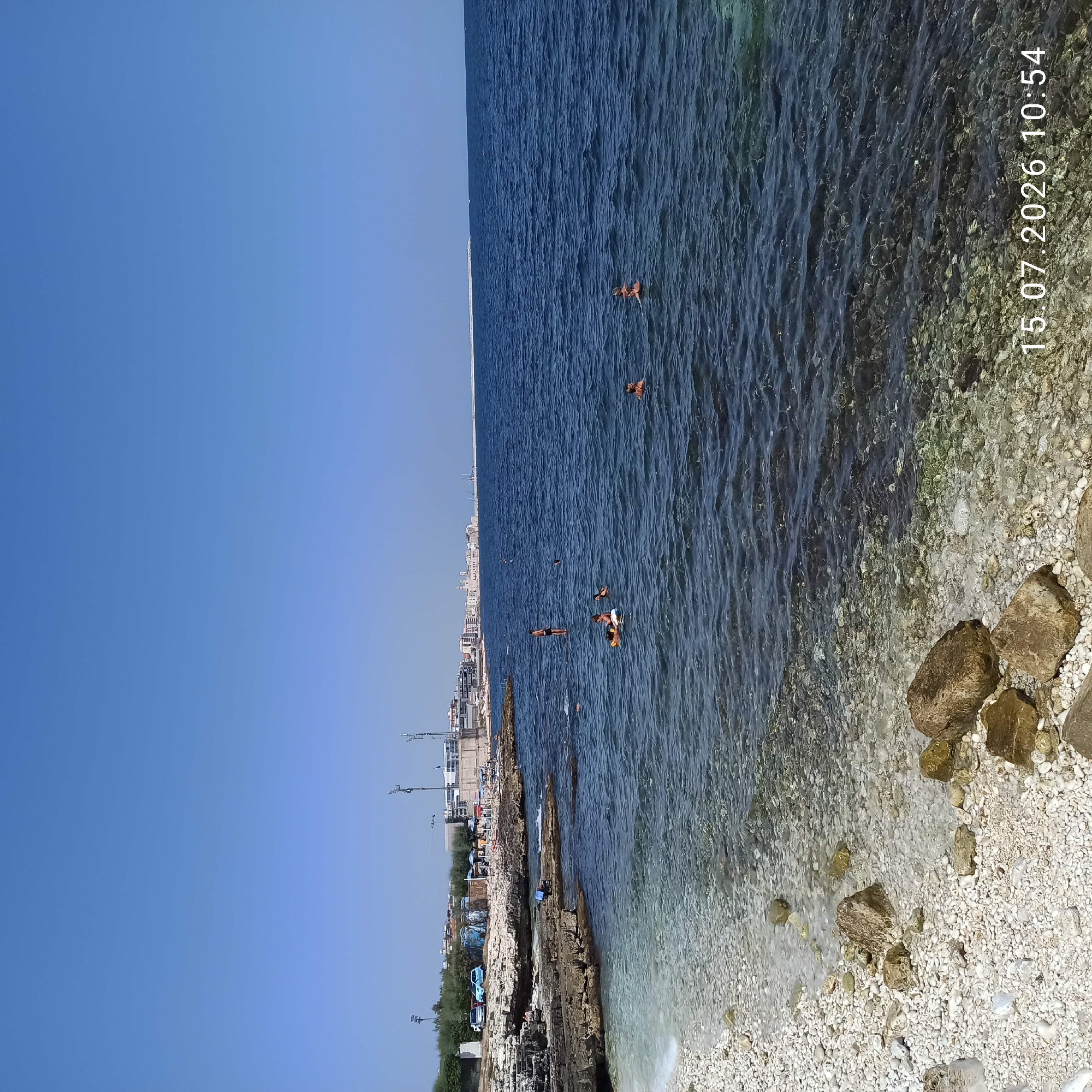 Sunny morning at Molfetta's rocky shore, people in and out of the water