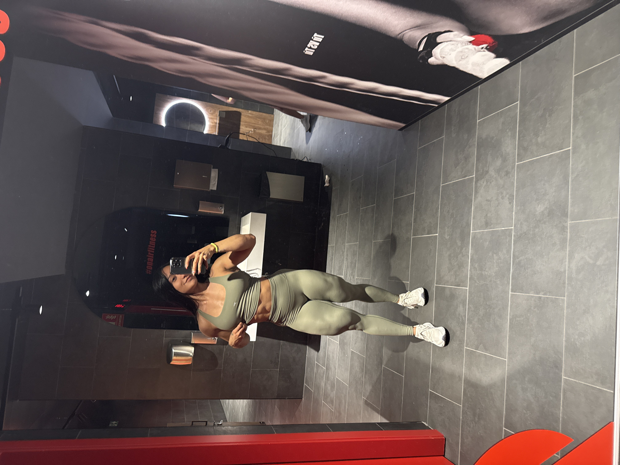 Mirror selfie in a Madrid gym bathroom, green athletic fit.
