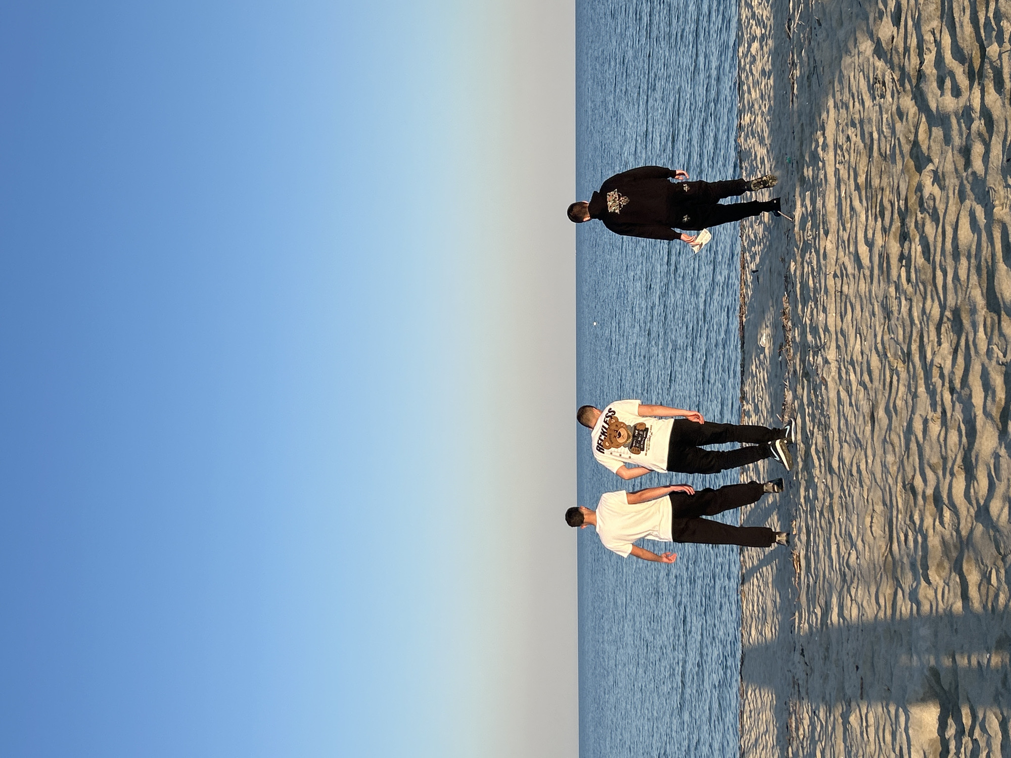 Three men gather on Greek beach under clear skies