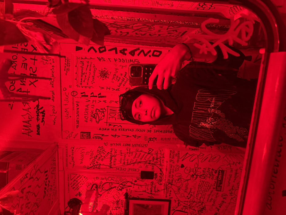 Hooded figure takes mirror selfie in graffiti-covered Mexico City room