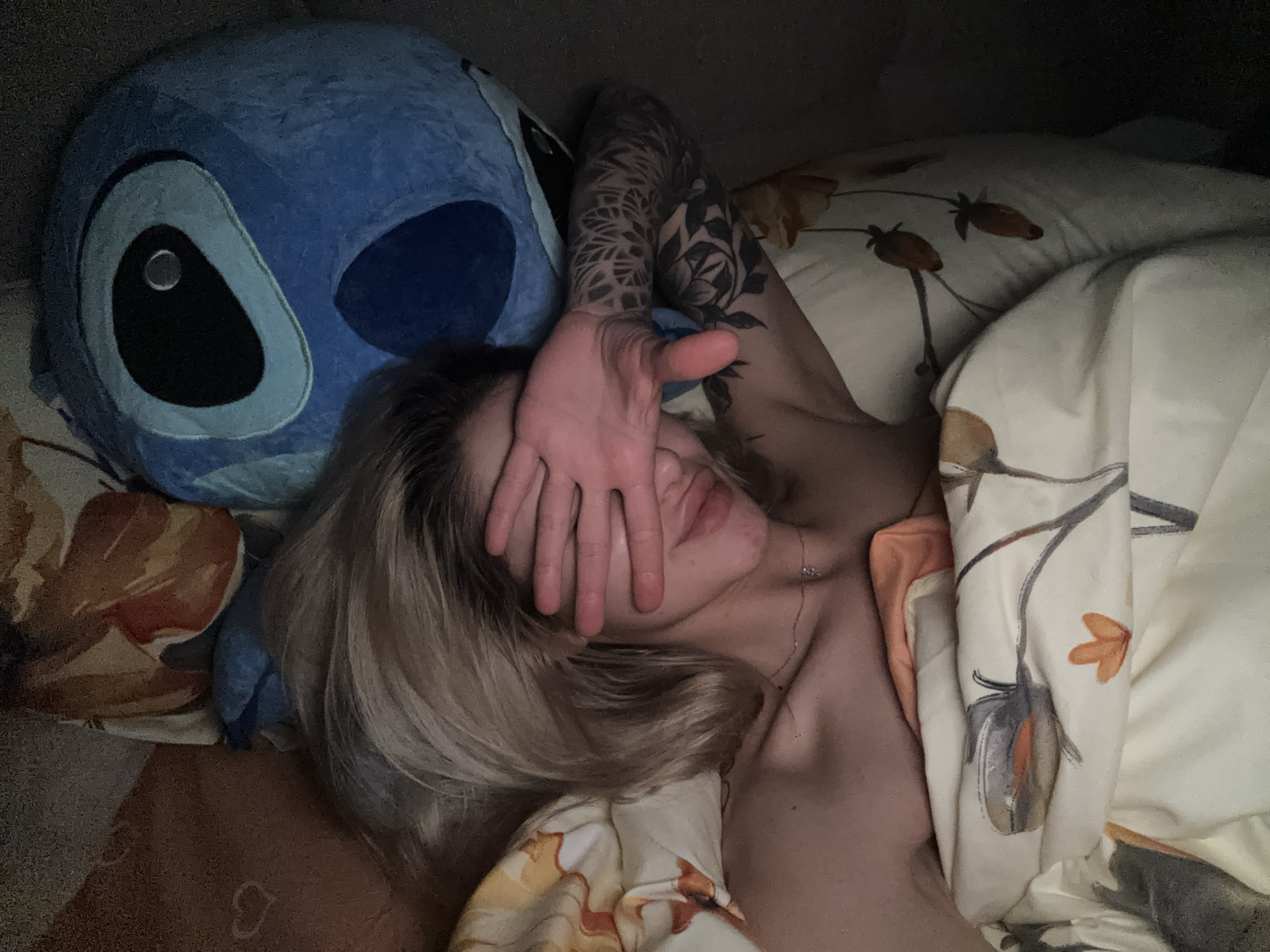 Person with tattoo rests in bed beside blue plush toy