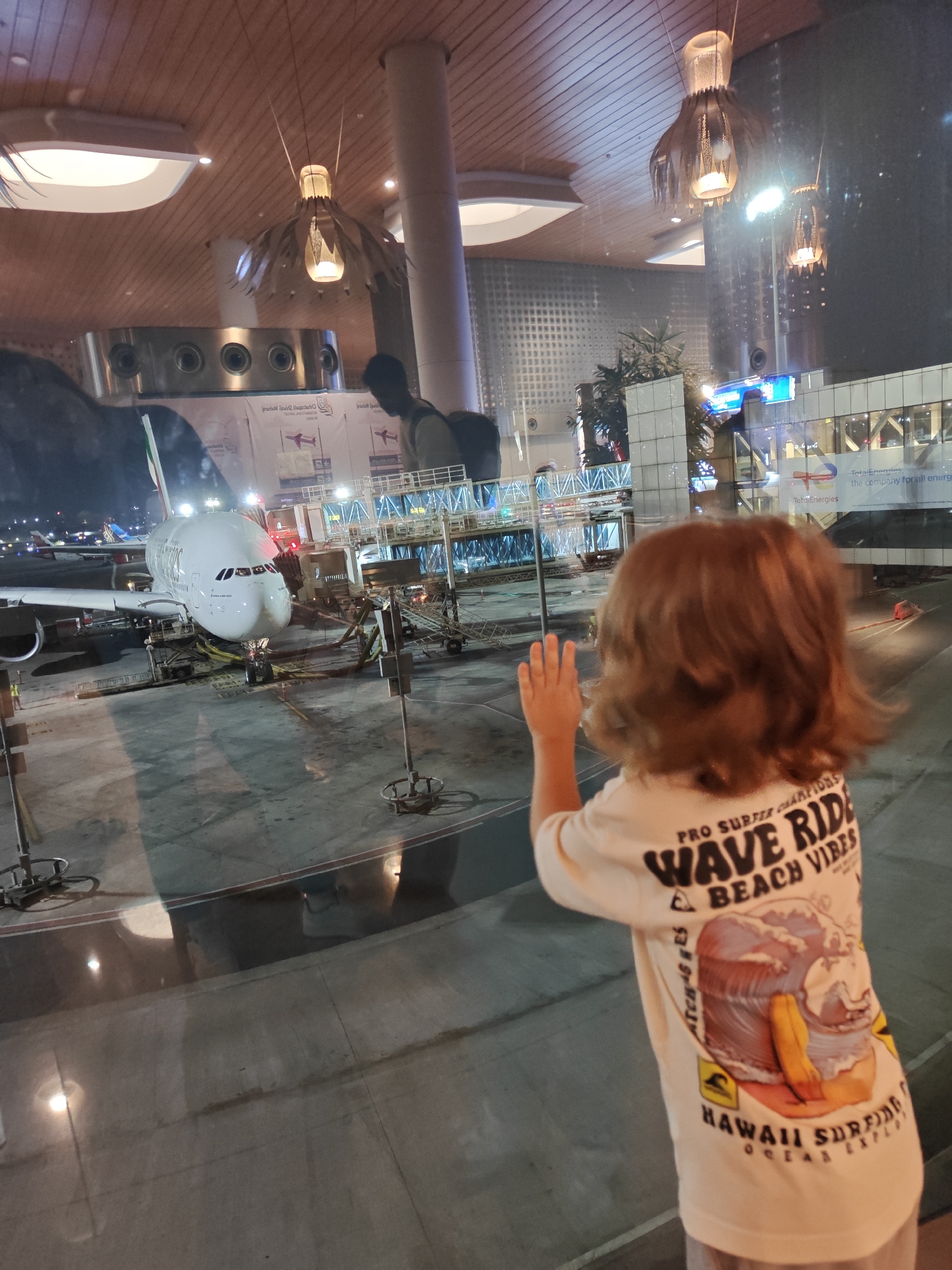 Child in surfing shirt gazes through Mumbai airport window