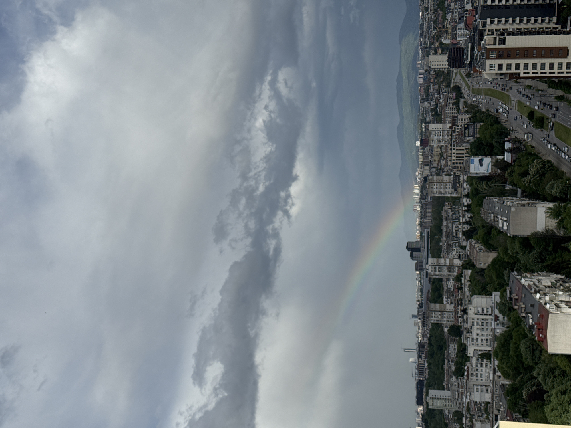 Rainbow appears over dense urban cityscape amid cloudy afternoon