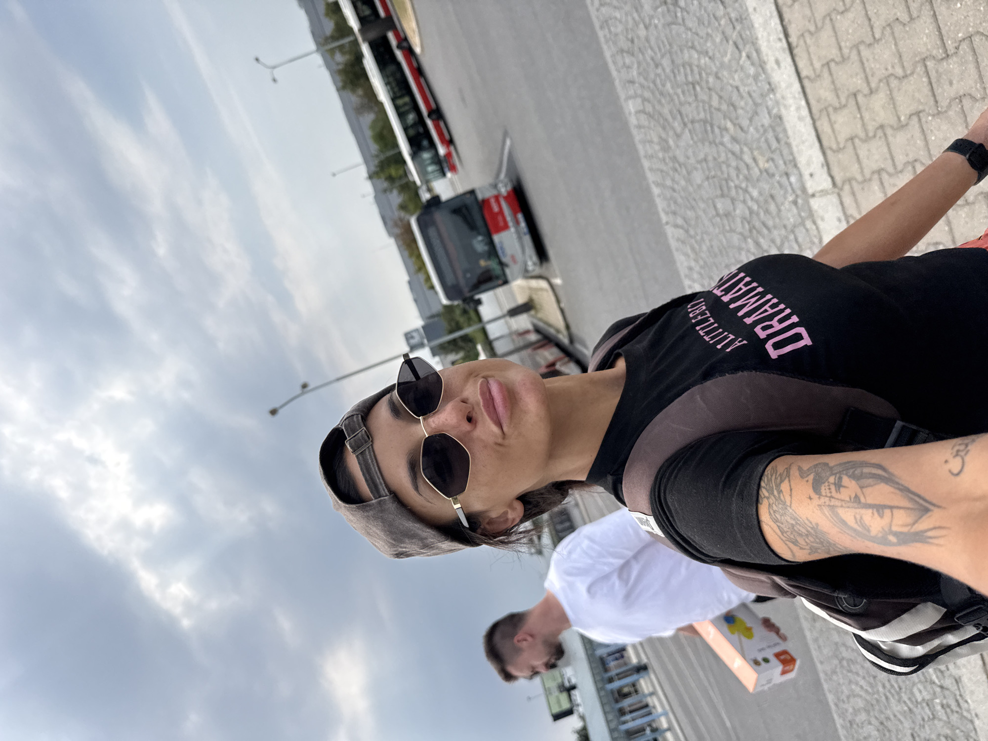 Selfie against a cloudy Prague sky, backpack and tattoo in view