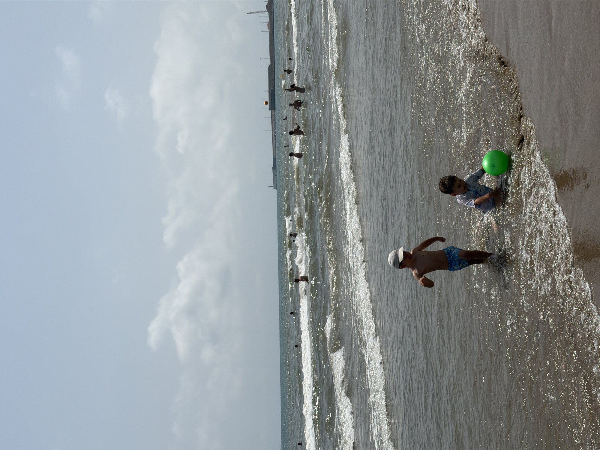 Crowded beach day with swimmers, kids, and street scenes nearby