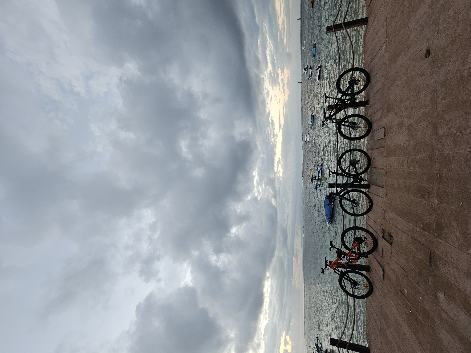 Cyclists pause at Sanur Beach boardwalk under a cloudy evening sky.