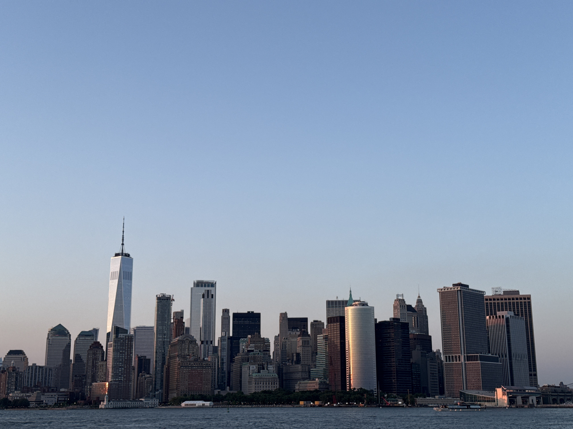Lower Manhattan skyline glows at sunset around One World Trade Center.