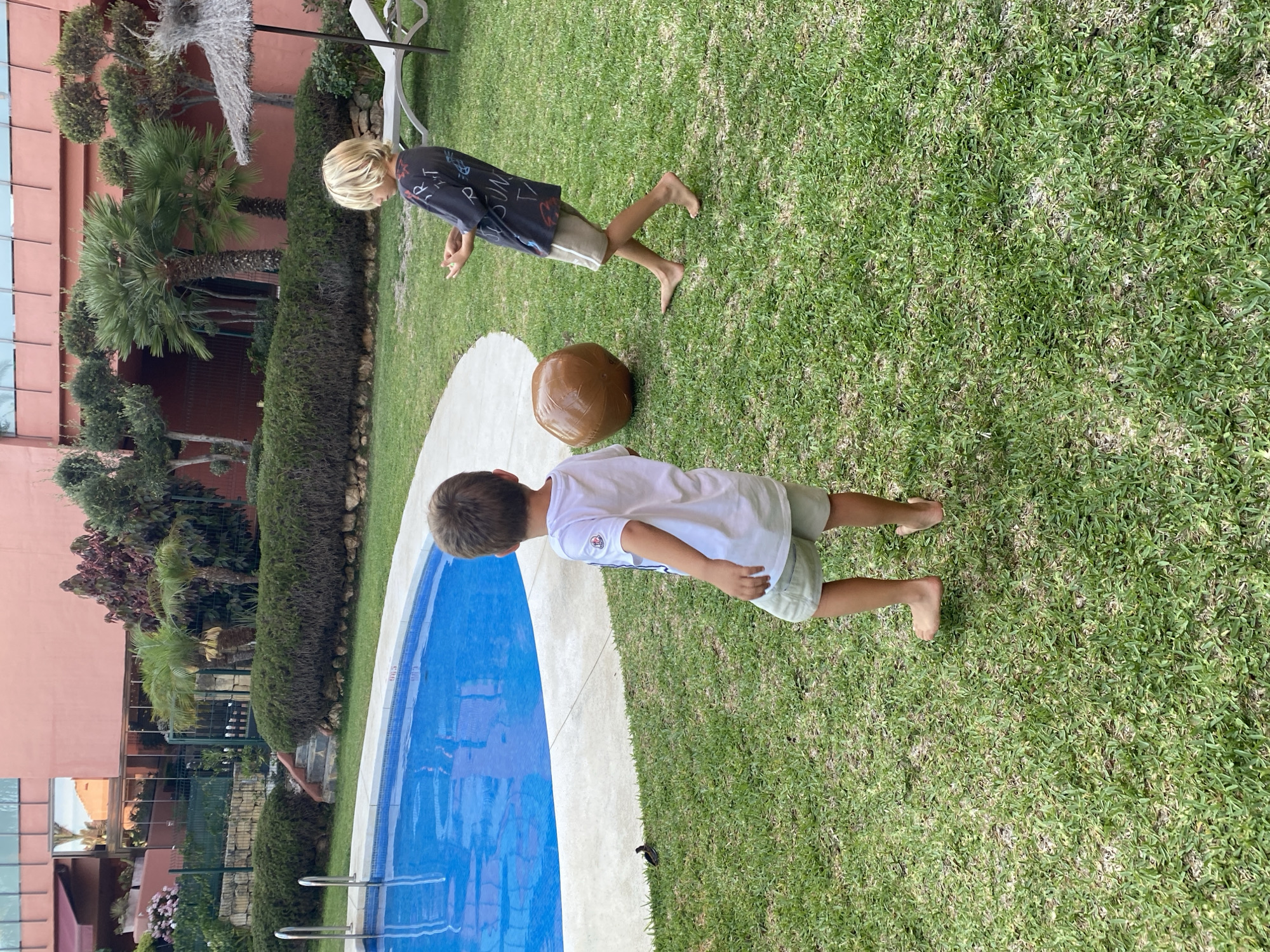 Kids playing with an inflatable ball by a backyard pool in Spain