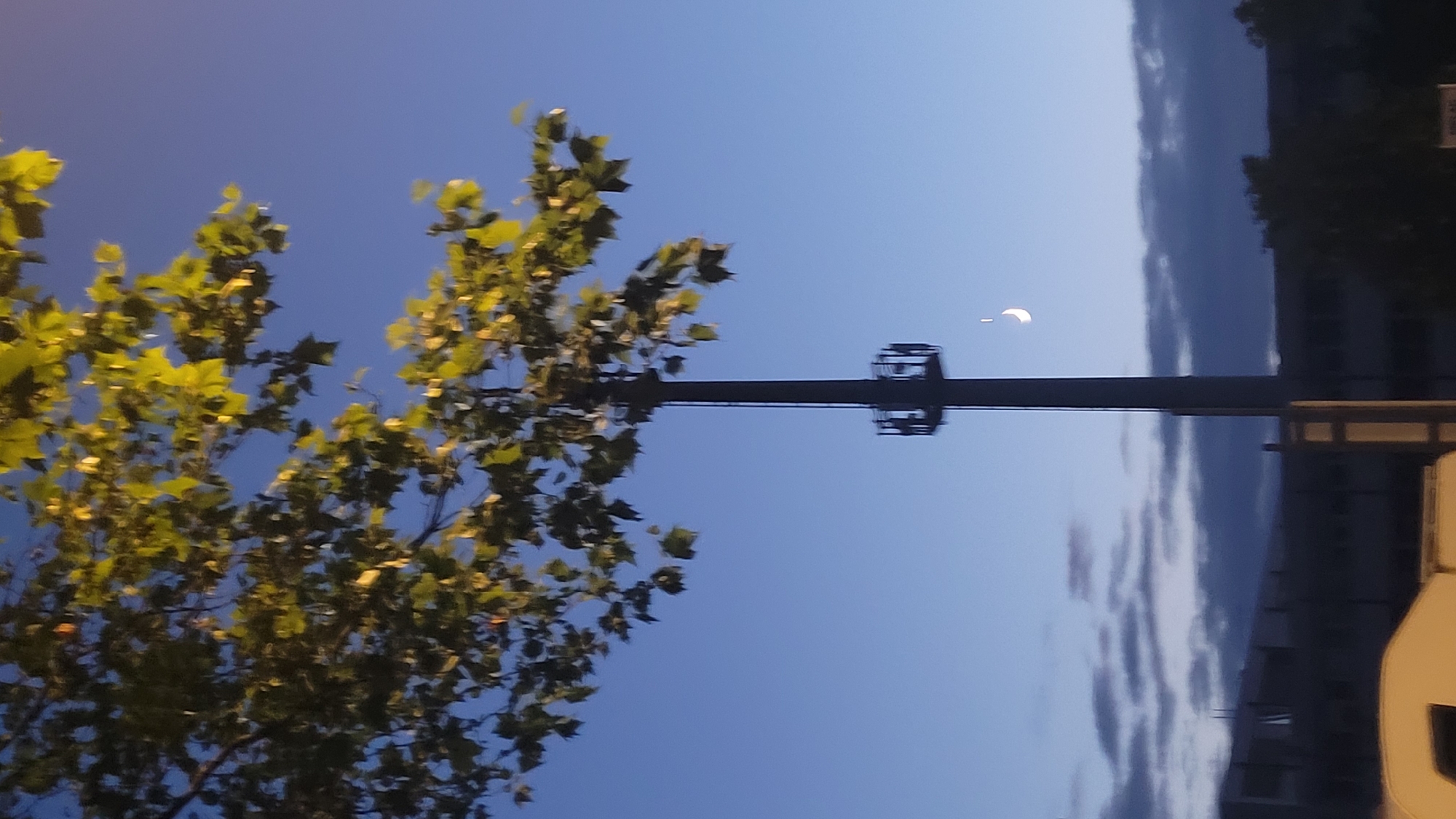 Crescent moon rises over a quiet neighborhood at dusk.