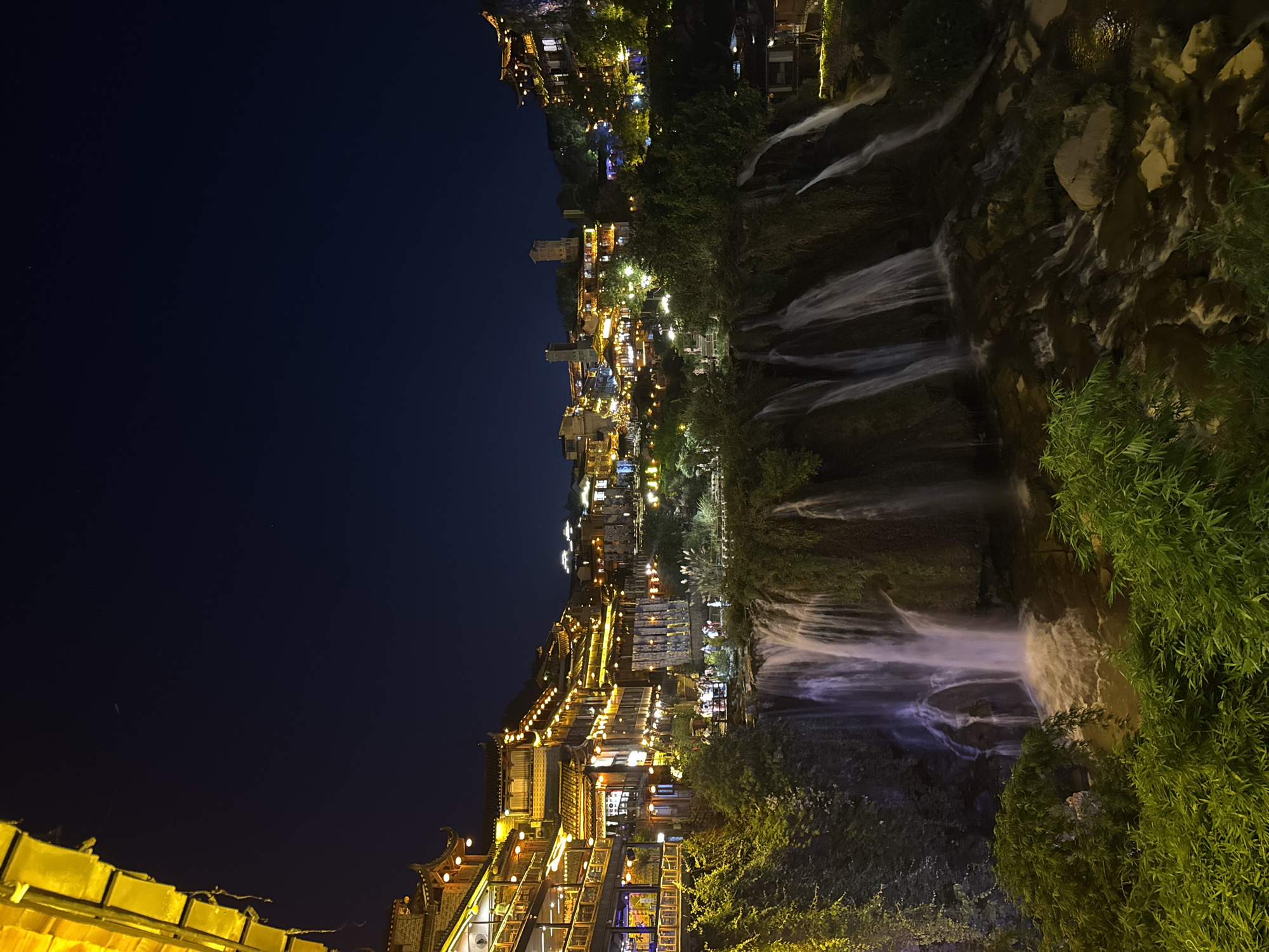 Furong Ancient Town glows at night above its cascading waterfall