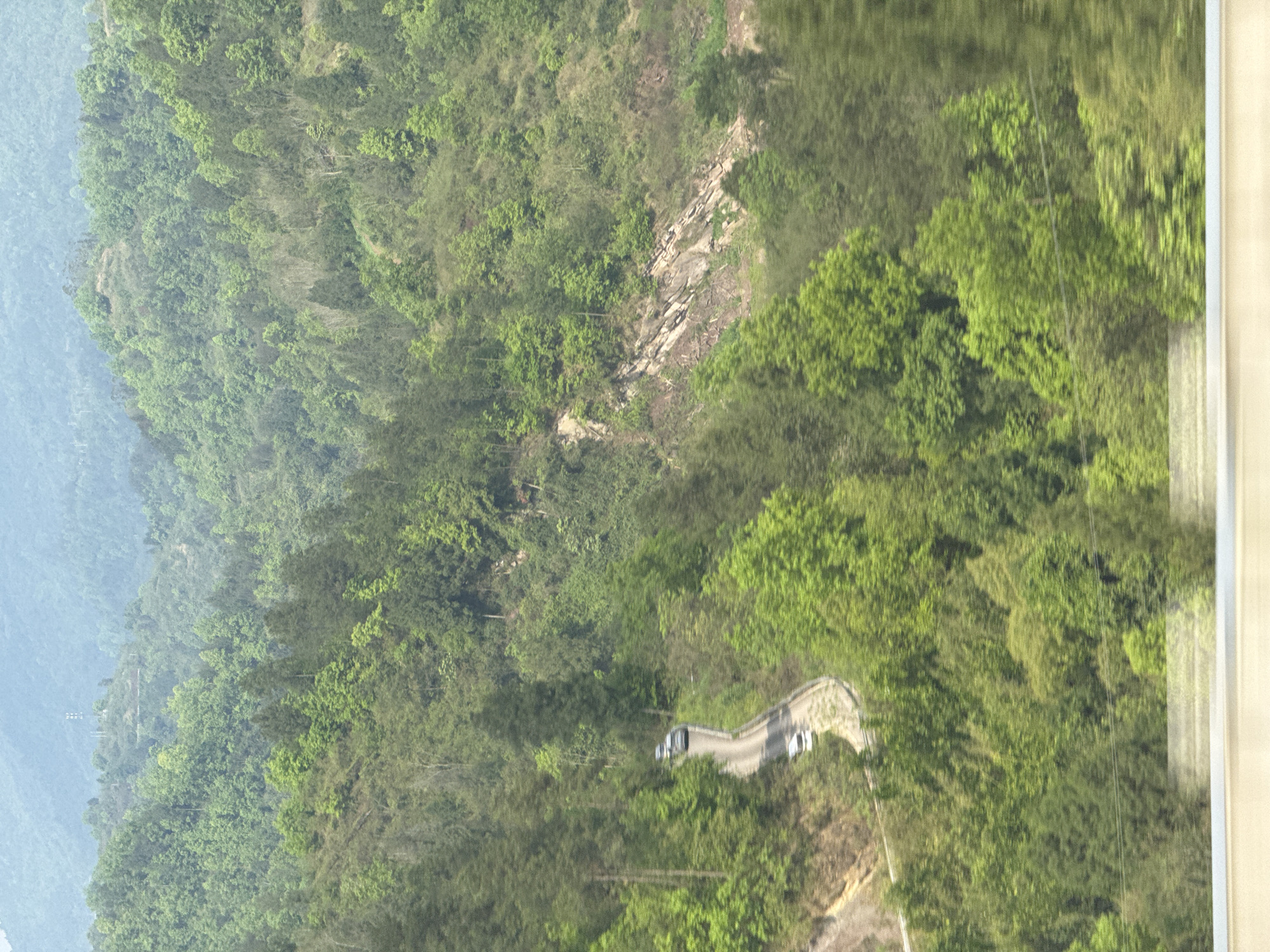 Vehicles navigate winding mountain road through dense forest in Dongwenquan