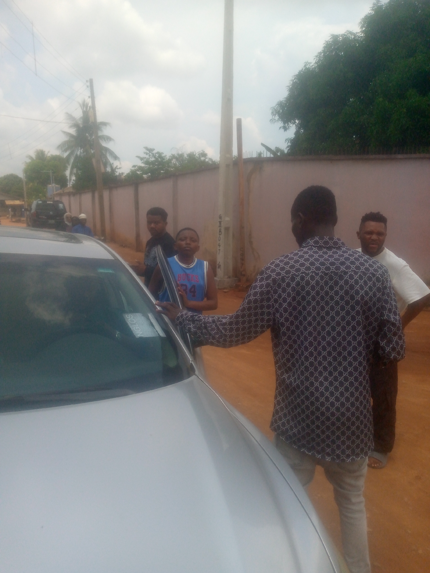 Film crew gathers around silver car in residential area