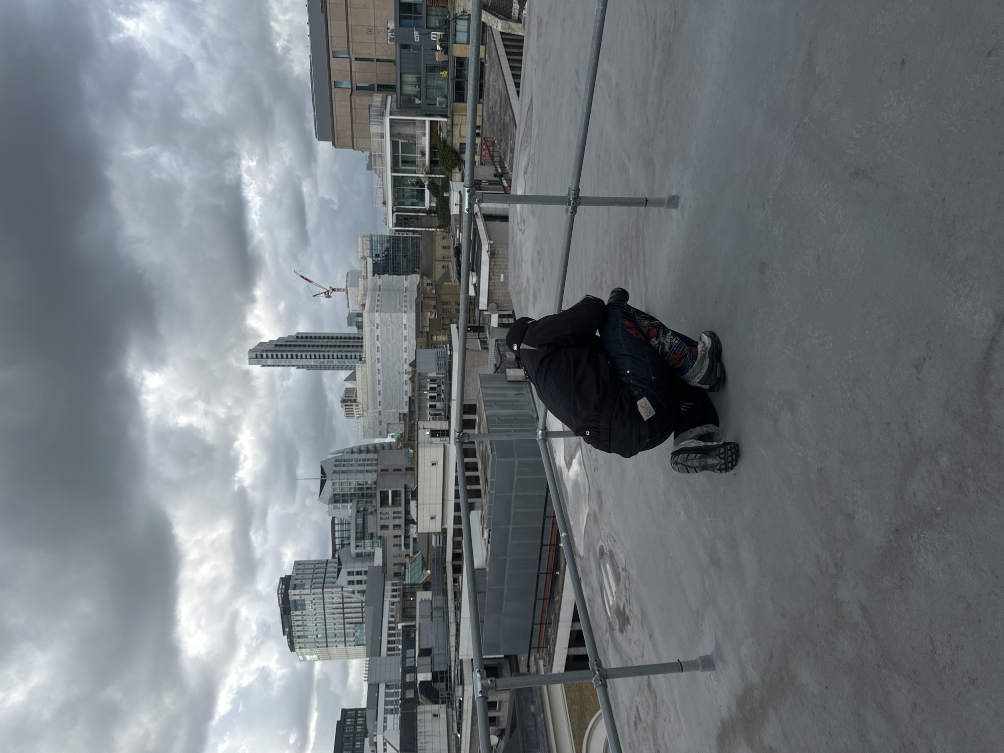 Person observed on London rooftop viewing cityscape during overcast afternoon