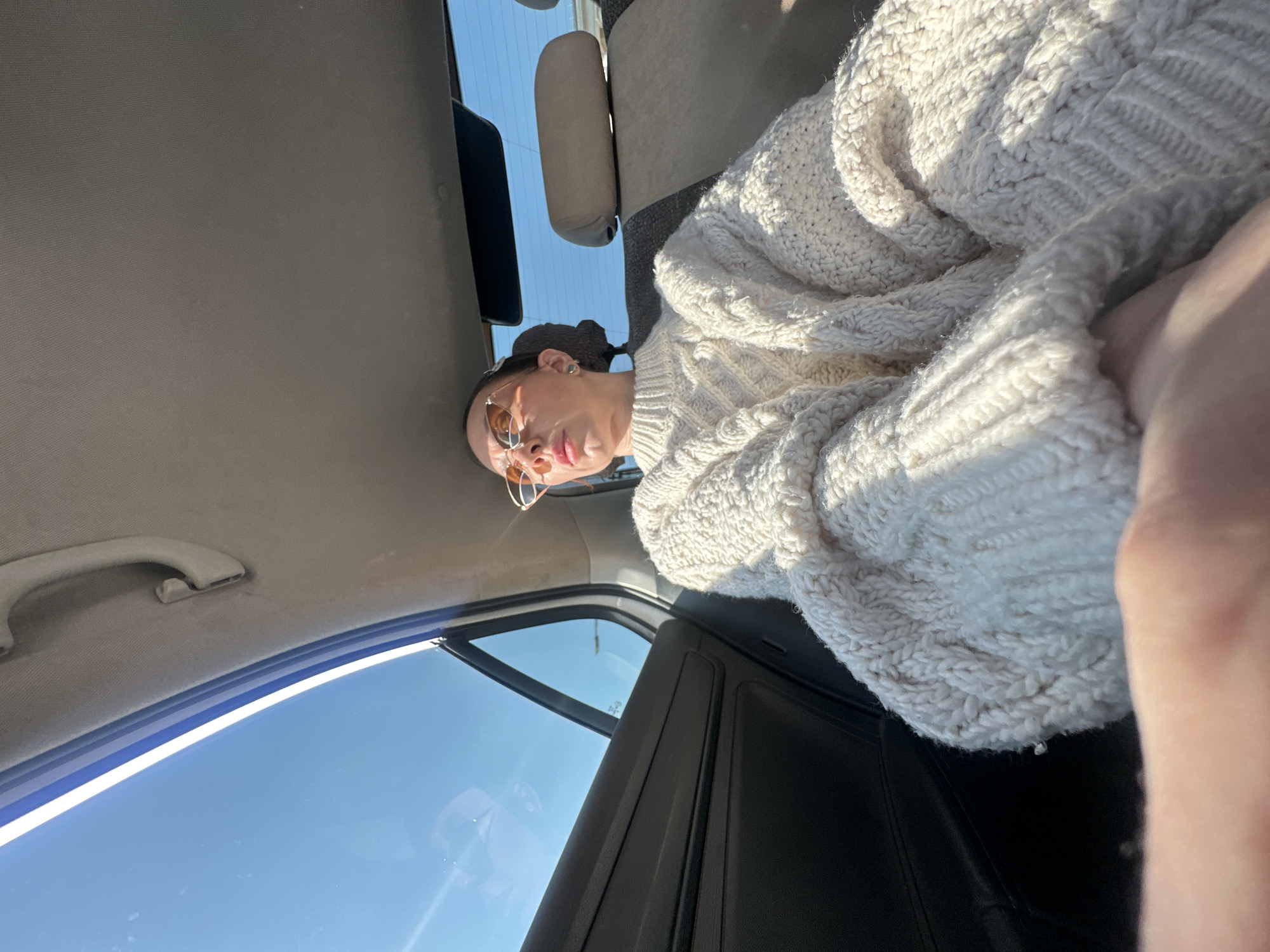 Person in sunglasses, white sweater photographed inside car in Votkinsk