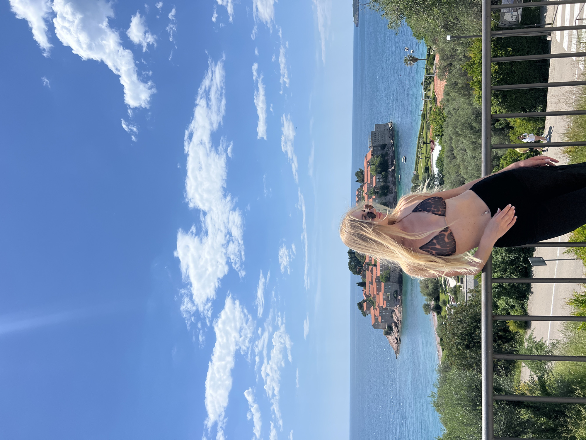 Woman poses on balcony overlooking Sveti Stefan, Montenegro