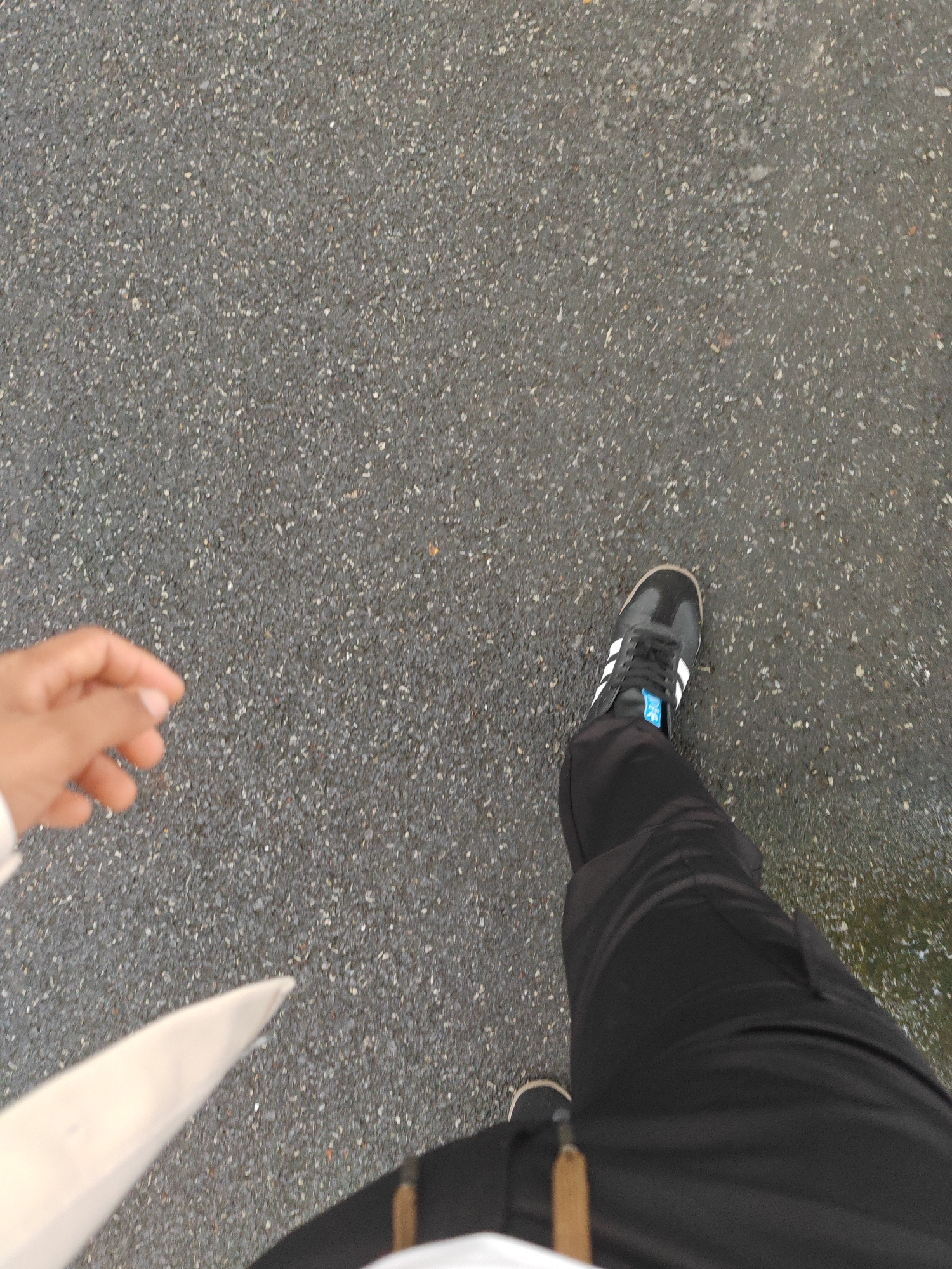 Person in black Adidas sneakers walks on asphalt in Jiangning
